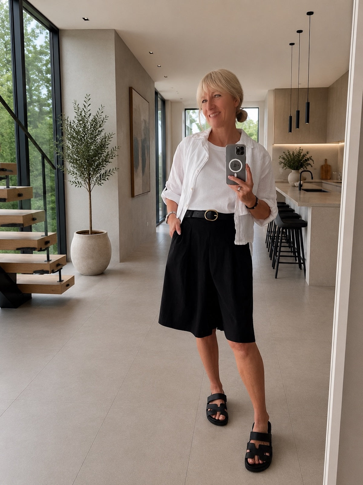 Sportlich-elegante Damen Bermuda Lola in Schwarz, kombiniert mit einer lockeren weißen Sommerbluse für eine perfekt definierte Silhouette, Ganzkörperansicht im exklusiven Store-Ambiente