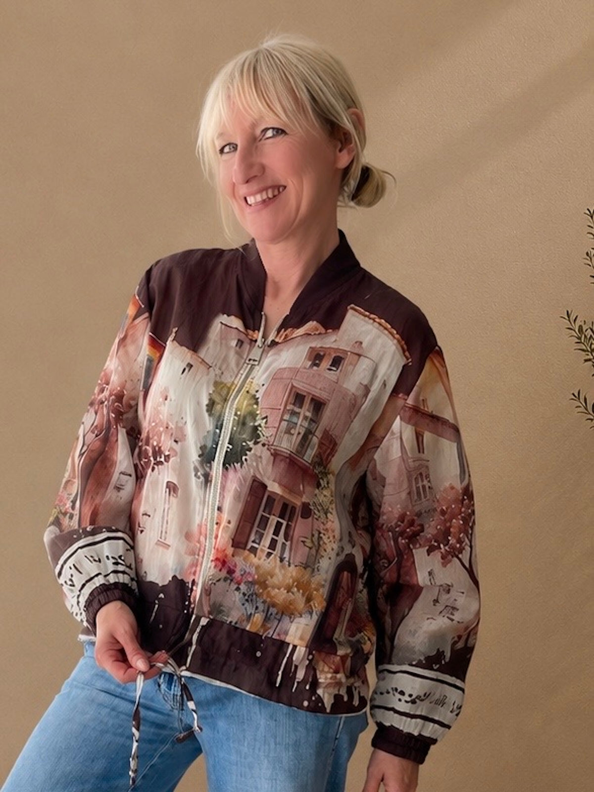 Blondes Modell (1,68 m) trägt eine sehr leichte, transparente Blouson-Jacke mit einem aufwendigen Art-Print in Brauntönen, lässig kombiniert mit einer weiten blauen Jeans