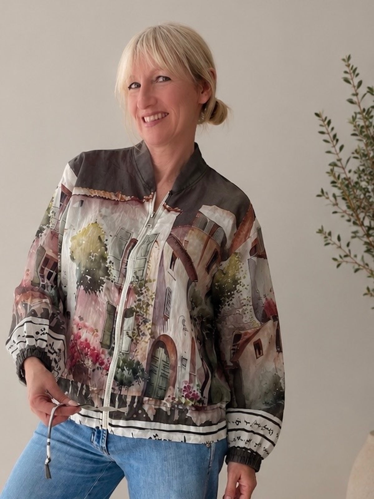 Blondes Modell (1,68 m) trägt eine sehr leichte, transparente Blouson-Jacke in Khaki mit einem aufwendigen mediterranen Art-Print, sportlich kombiniert mit einer weiten blauen Jeans.