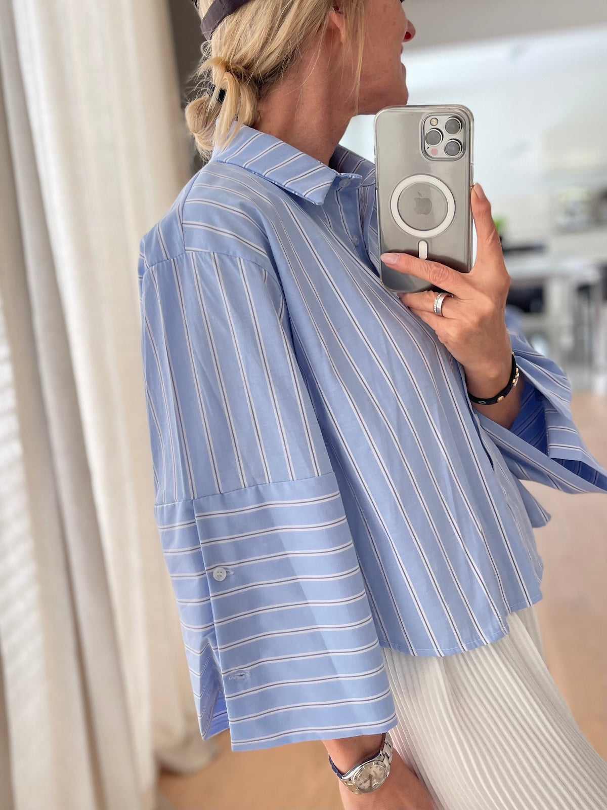 Silke von SILKE MODEN präsentiert die hellblau-weiß gestreifte Bluse Isabella im lässigen Boxy-Fit mit weiten Ärmeln, sportlich kombiniert mit einem hellen Rock und einer dunklen Cap beim Spiegel-Selfie, side