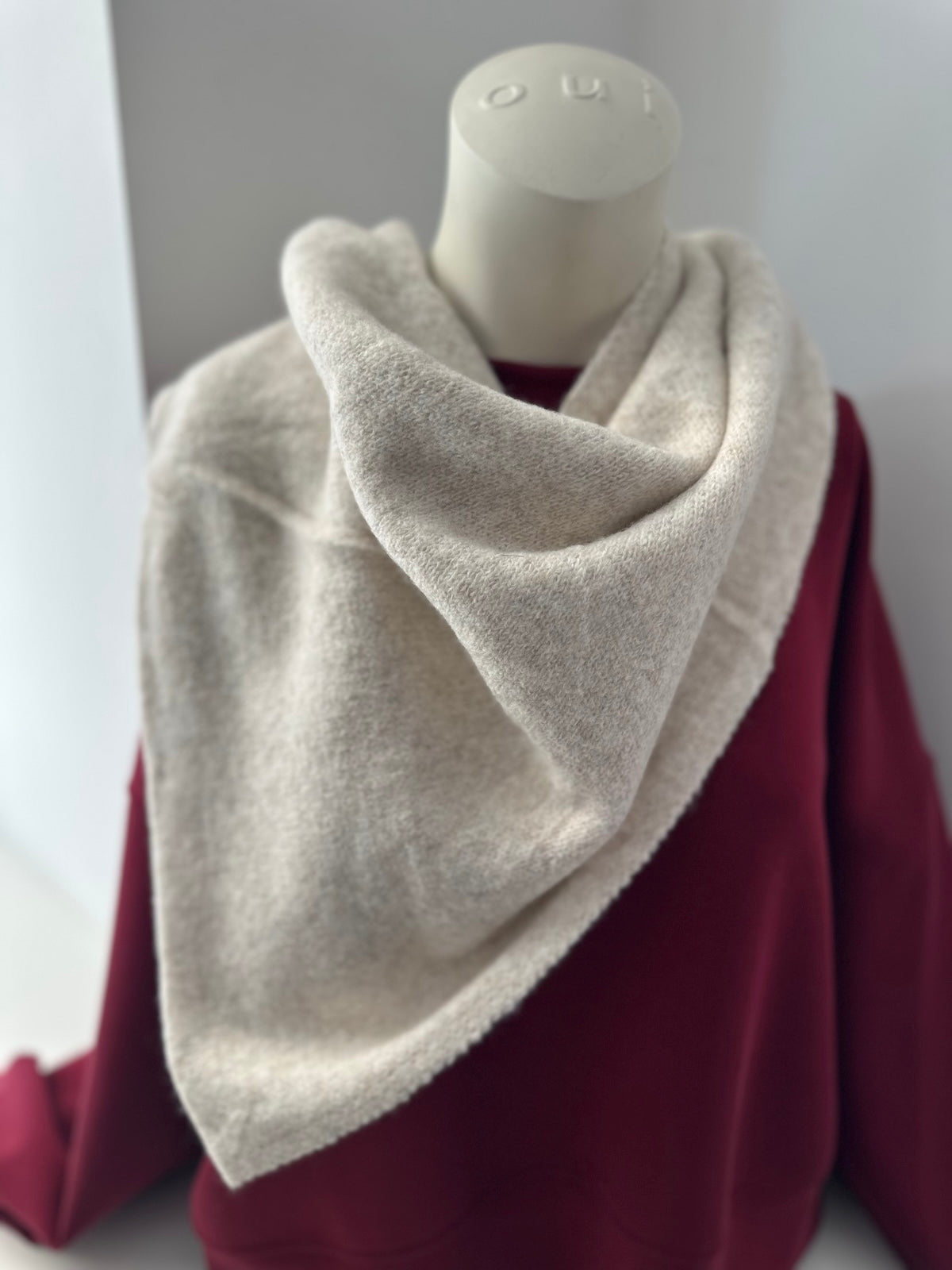 Schal aus den Beigefarbenen Accessoire-Set Alma, bestehend aus strukturiertem Dreieck-Schal und Mütze, stilvoll kombiniert auf einem bordeauxroten Oberteil.