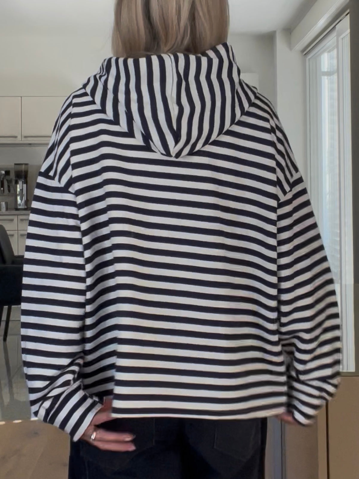 Rückansicht des gestreiften Hoodies Thea in Blau-Creme, die das strukturierte Volumen, die überschnittenen Schultern und den edlen Fall der Kapuze demonstriert.