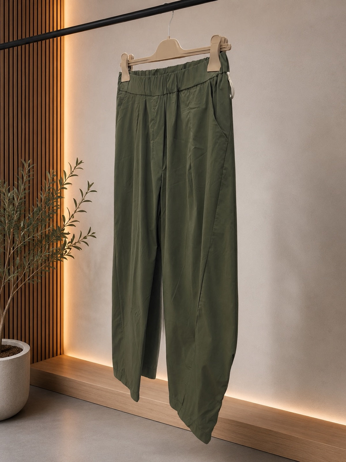 Produktaufnahme der Hose Elisa in Grün auf einem Holzkleiderbügel zur Veranschaulichung der seitlichen Eingrifftaschen, des elastischen Bunds und des matt-strukturierten Materials.