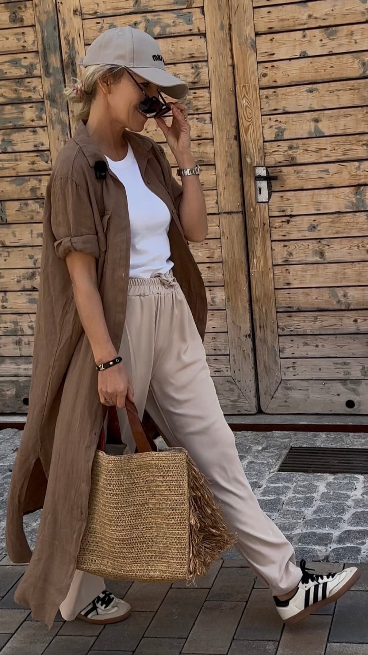 Unser Model im angesagten Layering-Look mit der weiten, stone-farbenen Sommerhose Tracy, einem weißen Shirt und einem langen braunen Hemdkleid, kombiniert mit Retro-Sneakern und einer Basttasche.