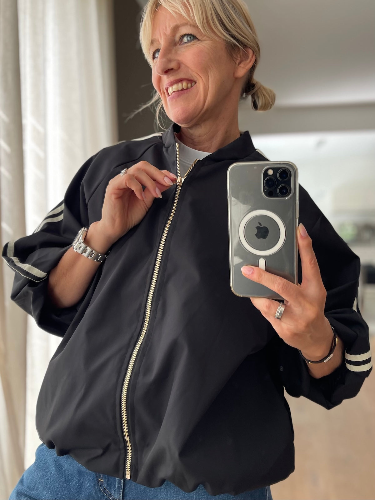 Sportlich elegante Blouson-Jacke Adi in Schwarz mit goldfarbenem Reißverschluss und markanten Kontraststreifen, getragen zu einer klassischen blauen Jeans.