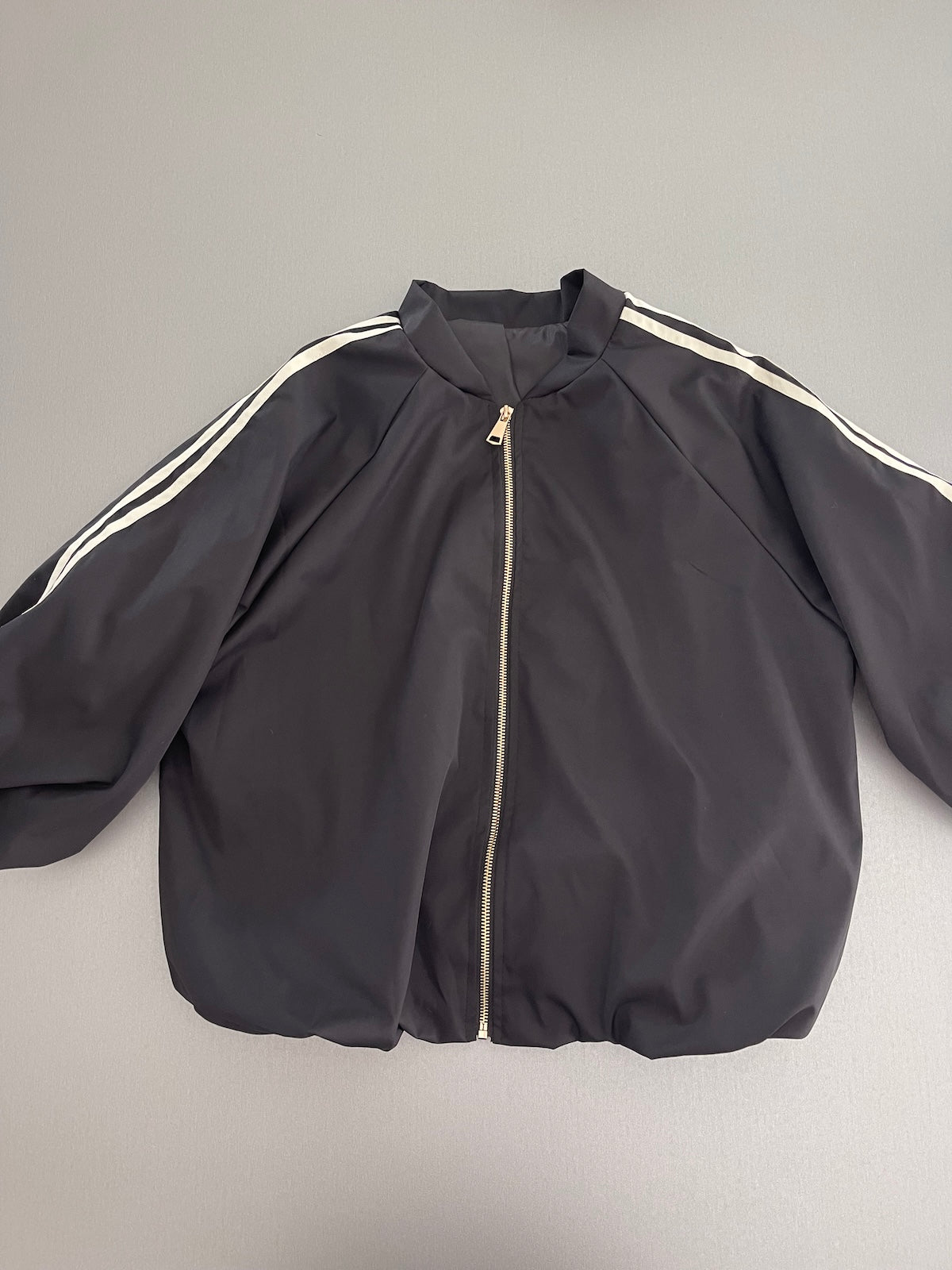 Frontansicht der kompakten schwarzen Jacke Adi im Blouson-Stil, die durch den formstabilen Elastikbund am Saum eine klare Silhouette definiert.