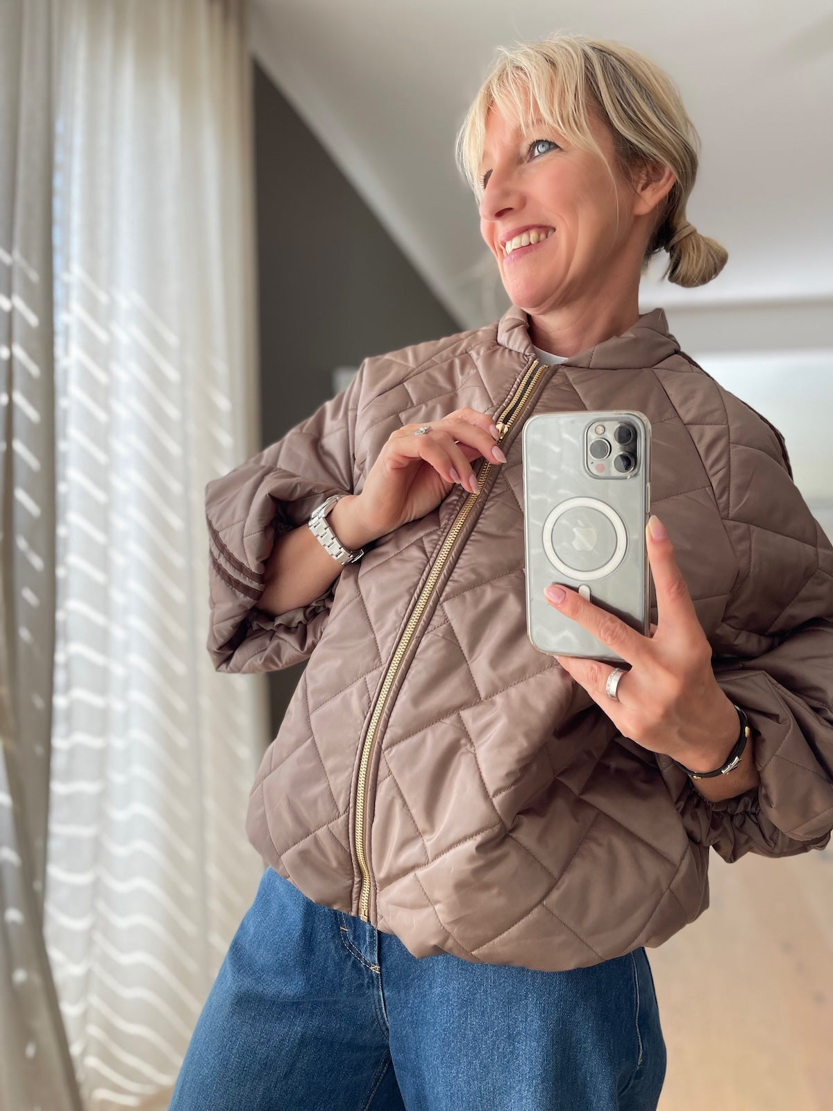 Sportlich elegante Blouson-Jacke Hannah in Taupe in markanter Stepp-Optik mit goldfarbenem Reißverschluss und braunen Ärmelstreifen, kombiniert mit einer blauen Jeans.