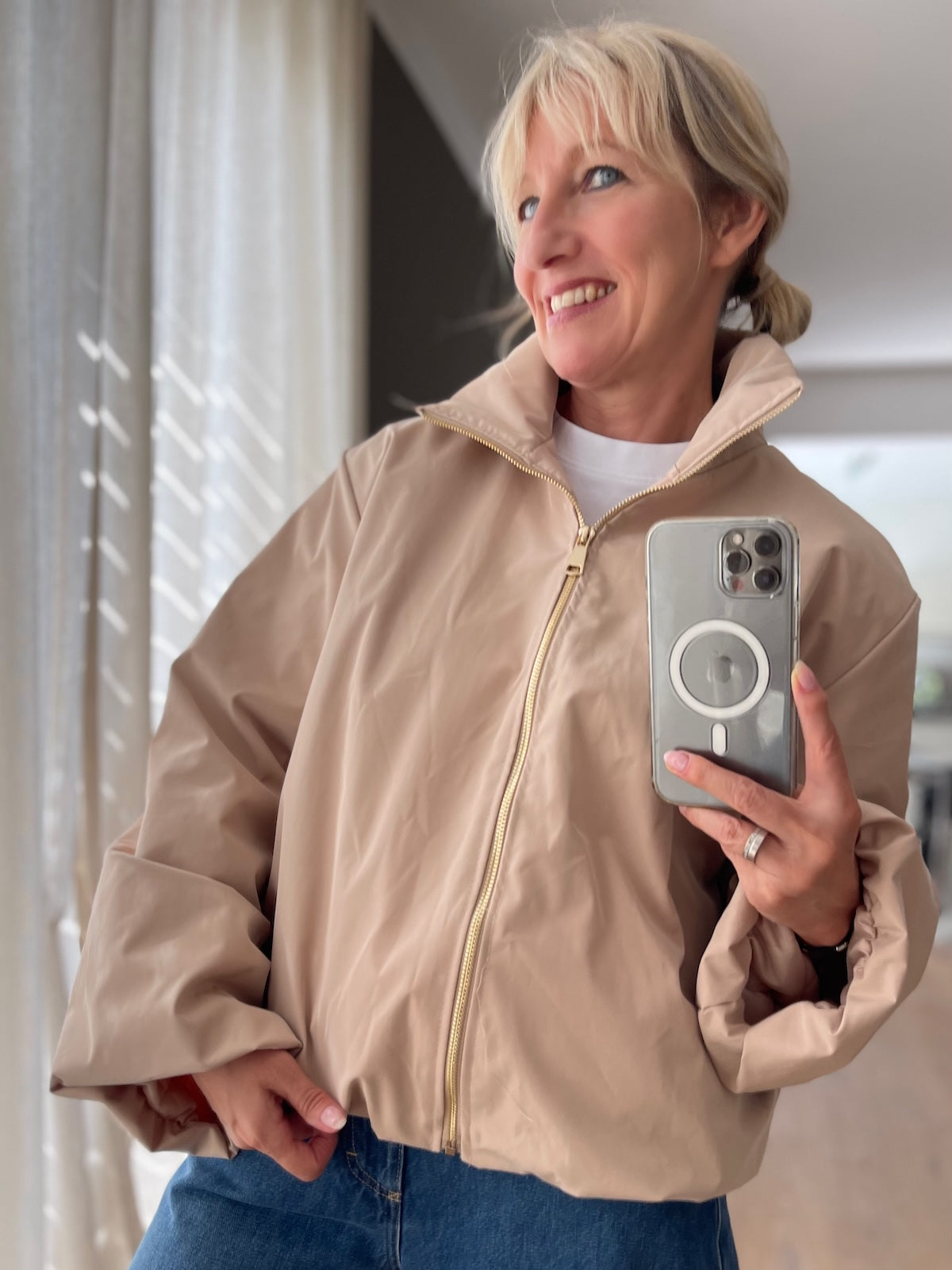 Dame präsentiert die elegante Jacke Sofia in Beige mit goldfarbenem Reißverschluss im modernen Boxy-Style.