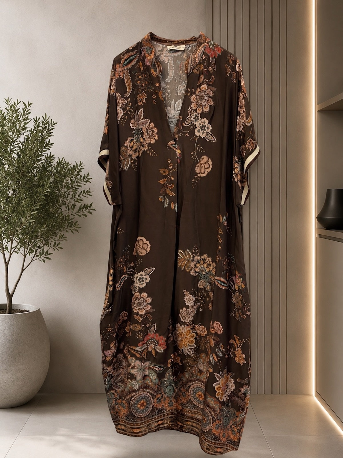 Produktaufnahme des drapierten Viskose-Seidenkleids Miranda in Dunkelbraun mit floralem Print auf einem Kleiderbügel vor einer hellen Studiowand.