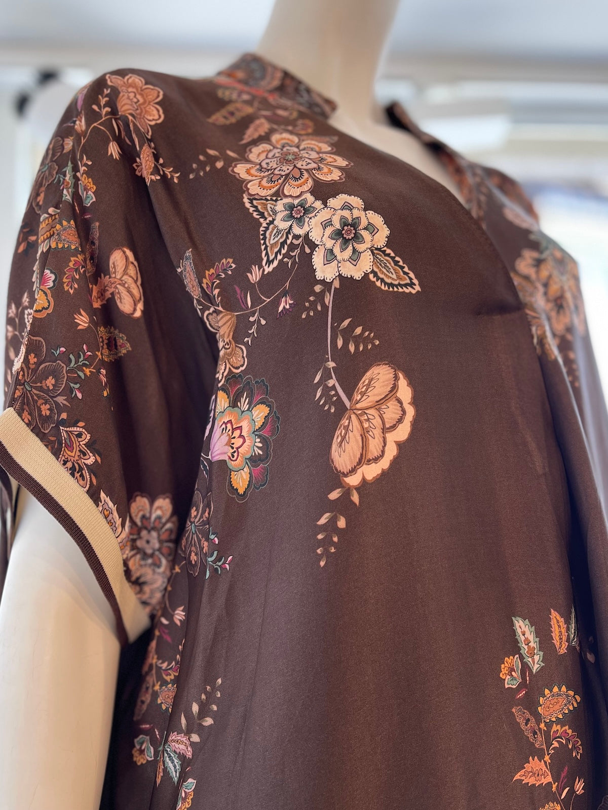 Nahaufnahme des Seidenkleids Miranda in Braun an einer Schaufensterpuppe zur Detaildarstellung des feinen Blumenprints, des V-Ausschnitts und des Kontrastbündchens am Ärmel.
