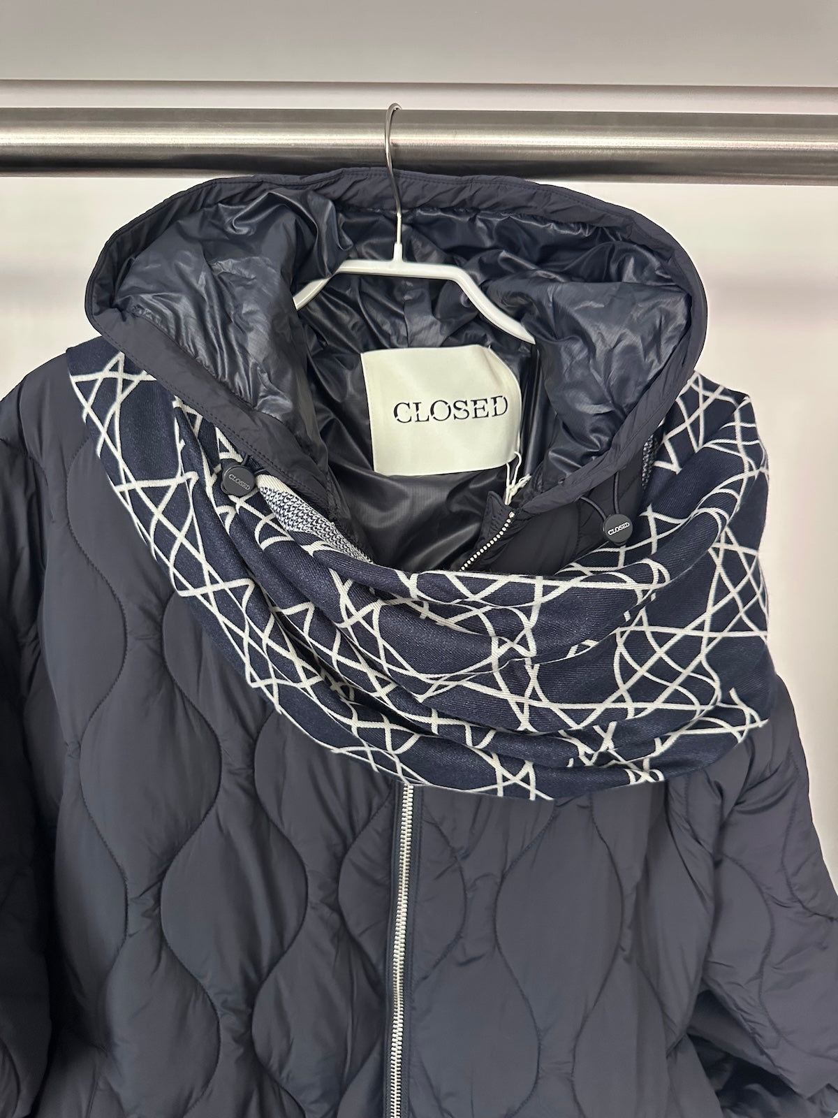 Exklusiver navyblauer Schal Noa mit weißem geometrischem Muster, strukturiert drapiert über einer dunklen Steppjacke.