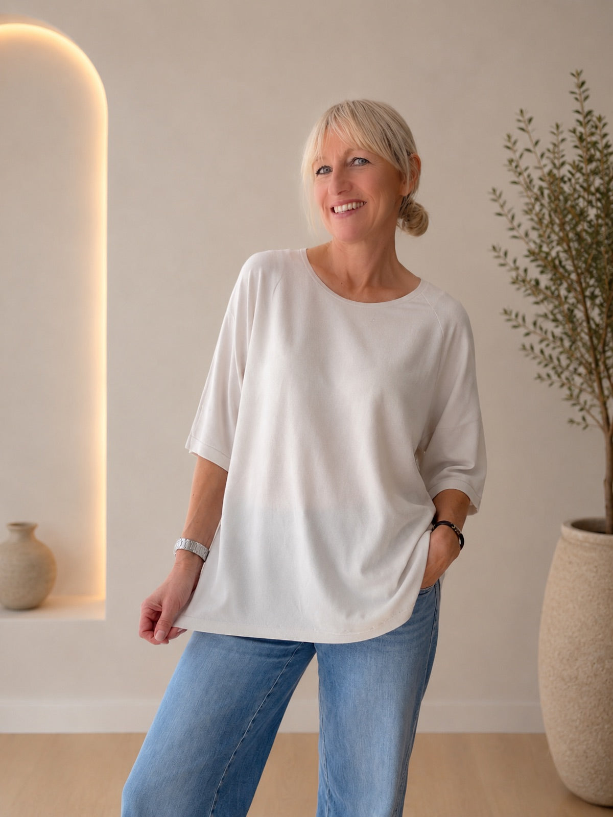 Lächelndes Model in einem weich fließenden, stone-farbenen Shirt Audrey mit halblangen Ärmeln vor hellem Hintergrund.