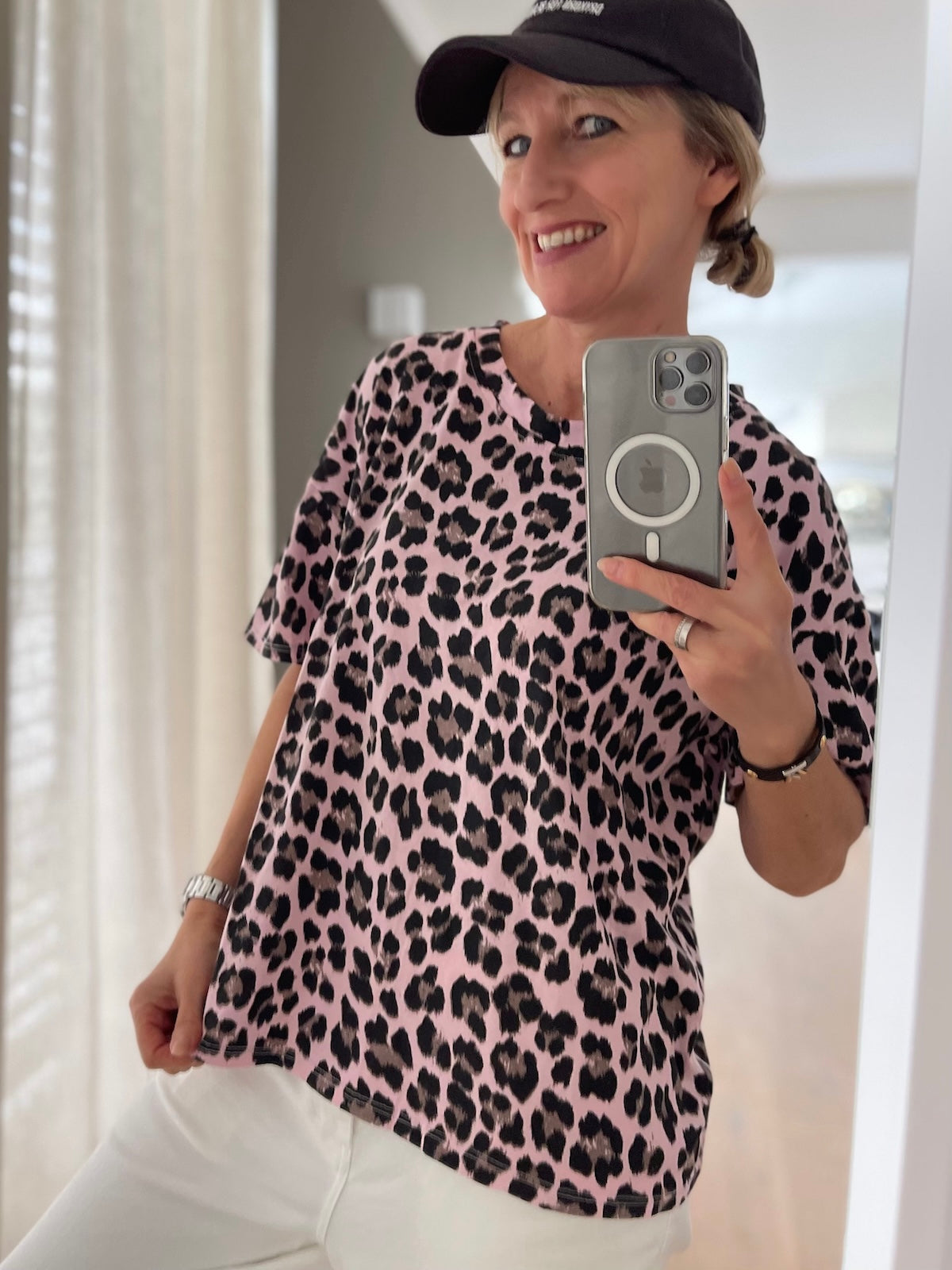 Side Nahaufnahme des roséfarbenen T-Shirts Bea mit schwarzem Leo-Muster, zu weißer Hose, Fokus auf Print und Schnitt.