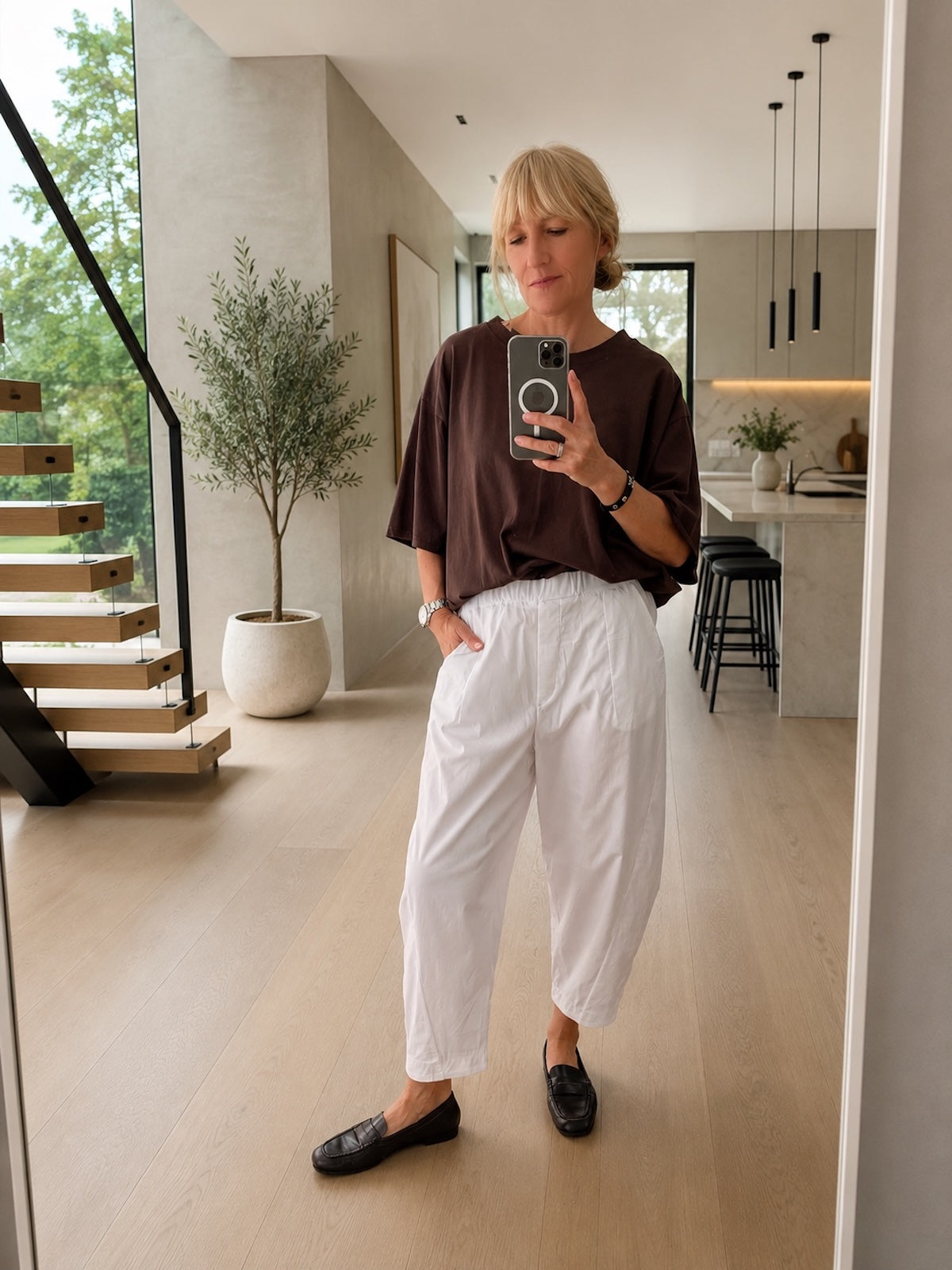 Sportlich-elegantes Damen Kurzarmshirt Emily in Schokobraun, kombiniert mit einer beigen High-Waist-Hose für eine perfekt definierte Silhouette, Ganzkörper-Ansicht im modern designten Verkaufsraum