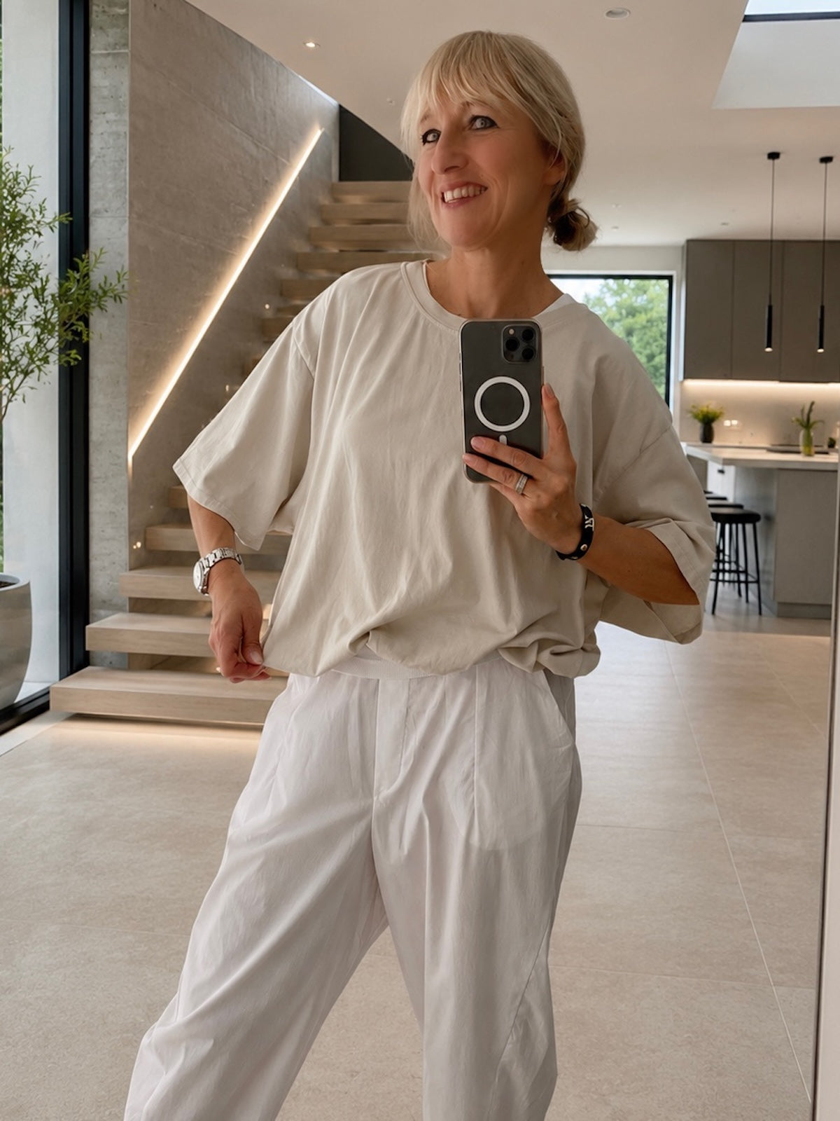 Sportlich-elegantes Damen Kurzarmshirt Emily in der hellen Nuance Stone, kombiniert mit einer weißen High-Waist-Hose für eine perfekt definierte Silhouette, Ganzkörper-Ansicht im minimalistischen Interieur