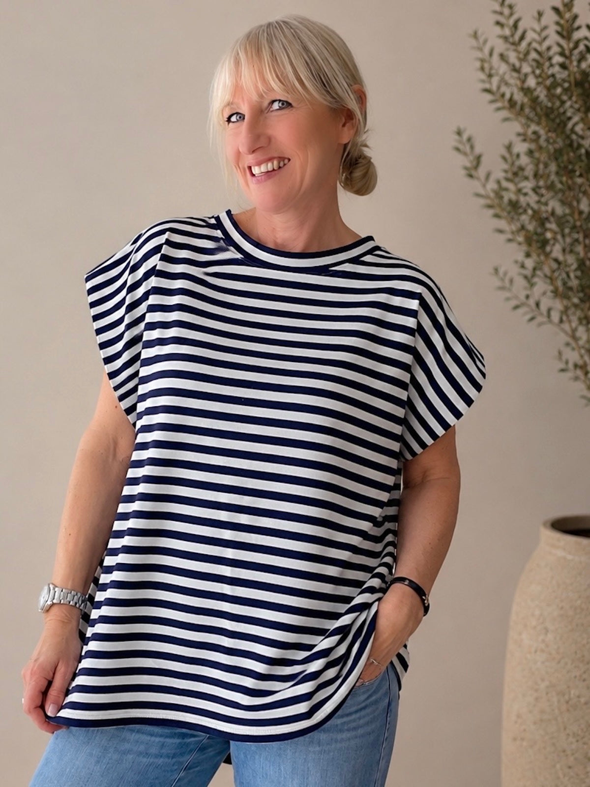 Lächelnde blonde Frau trägt das lässig fallende, blau-weiß gestreifte Shirt Laura mit überschnittenen Schultern kombiniert zu einer blauen Jeans.