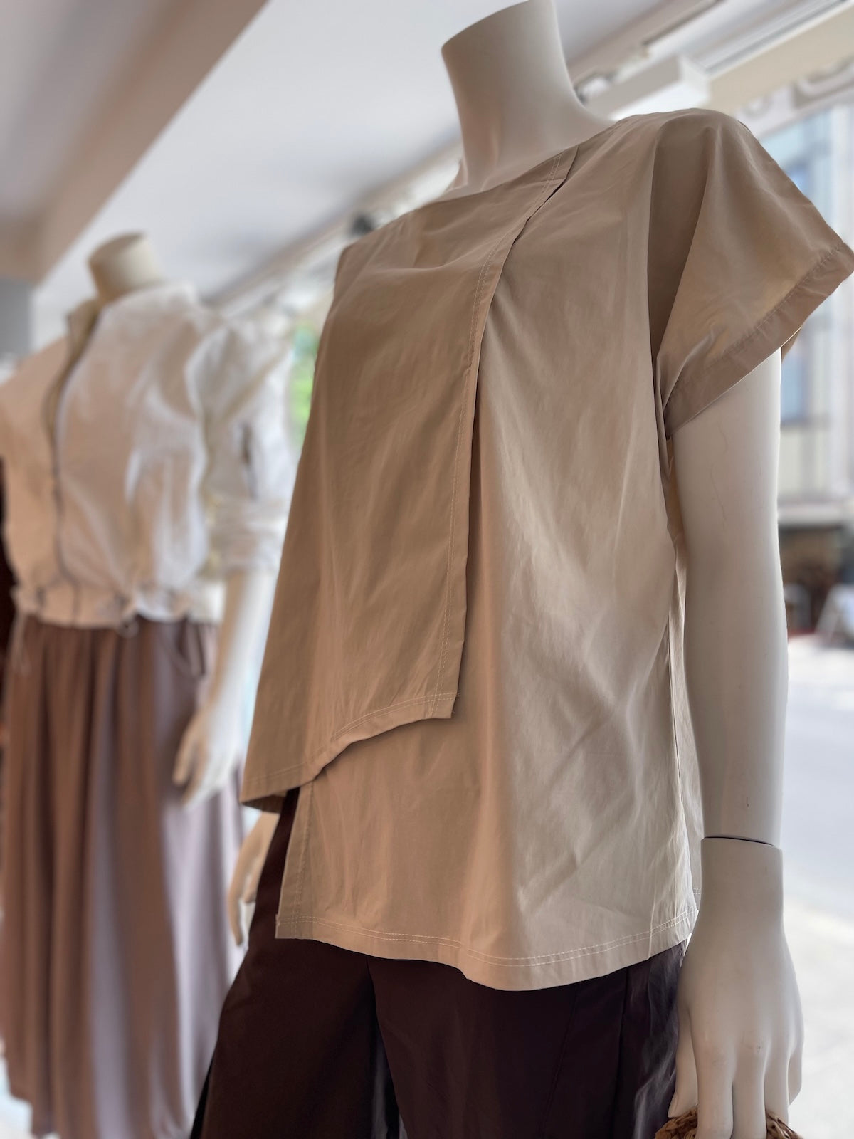 Clean geschnittenes Damen Shirt Marta in Stone mit geometrischem Layer-Look auf einer Schaufensterpuppe dekoriert im exklusiven Store-Ambiente