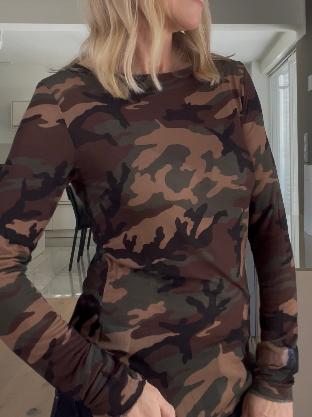 Eine modebewusste Frau trägt das edle Shirt Mona in Camouflage, perfekt gestylt mit körpernaher Silhouette und elegantem Ausschnitt zur dunklen Denim.