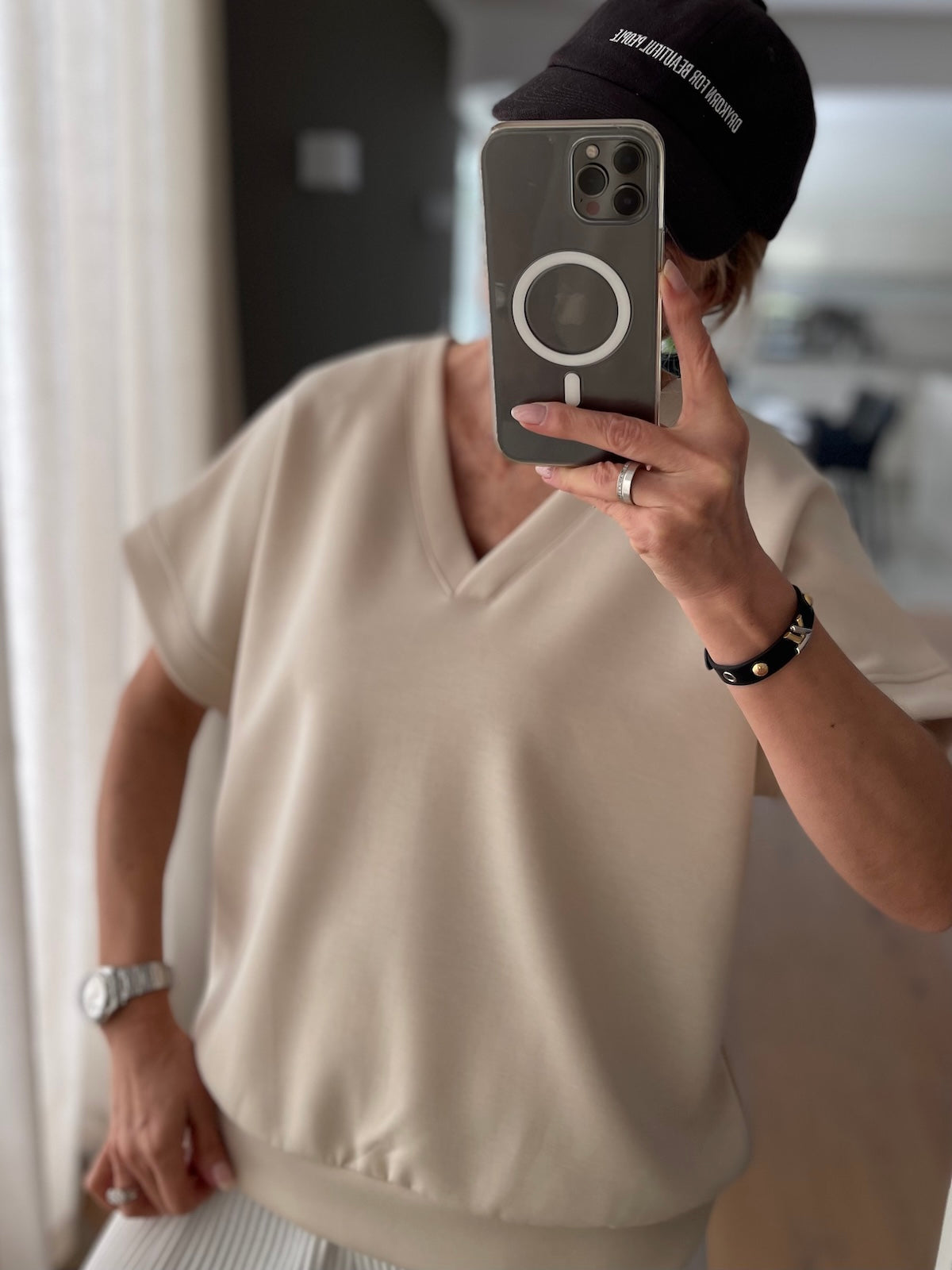 Nahaufnahme des beigefarbenen Shirts Christine, der hochwertige Viskose-Mix fällt weich und glatt, kombiniert mit einer schwarzen Kappe beim Spiegel-Selfie.