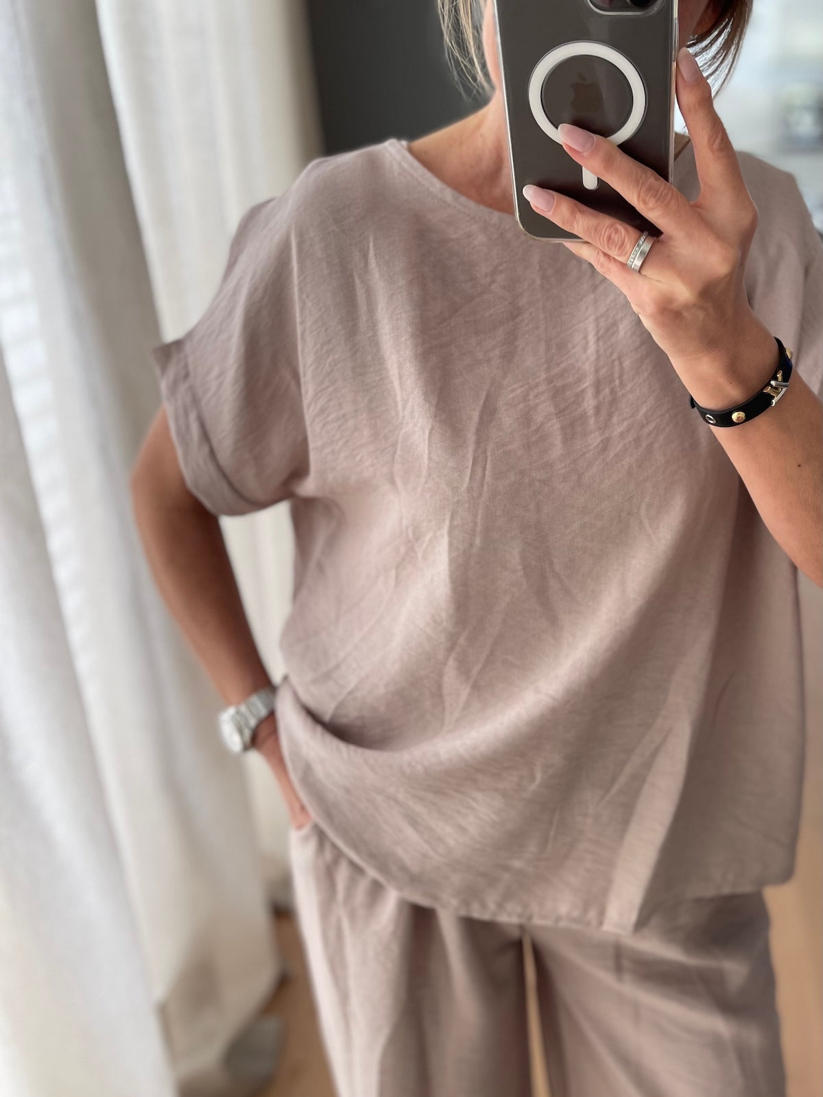 Nahaufnahme des taupefarbenen Shirts Diana, getragen von einem blonden Modell beim Spiegel-Selfie. Fokus auf die feine, strukturierte Viskose-Qualität und die umgeschlagenen Ärmel.
