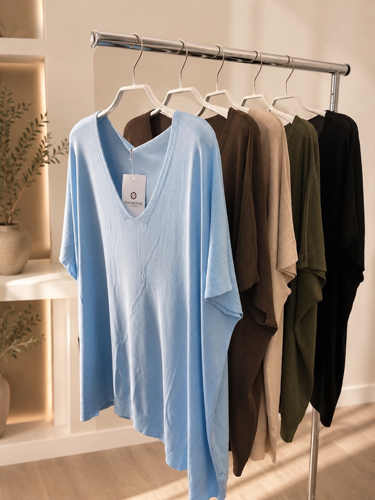 Eine Collage aus vier Produktbildern des weit fallenden Damen-T-Shirts Modell Maria. Es zeigt das Shirt in vier verschiedenen Farben: Hellblau, Schwarz, Beige-Taupe und Dunkelbraun, jeweils flach auf einem neutralen Hintergrund ausgebreitet, um die verfügbaren Farbvarianten zu präsentieren.