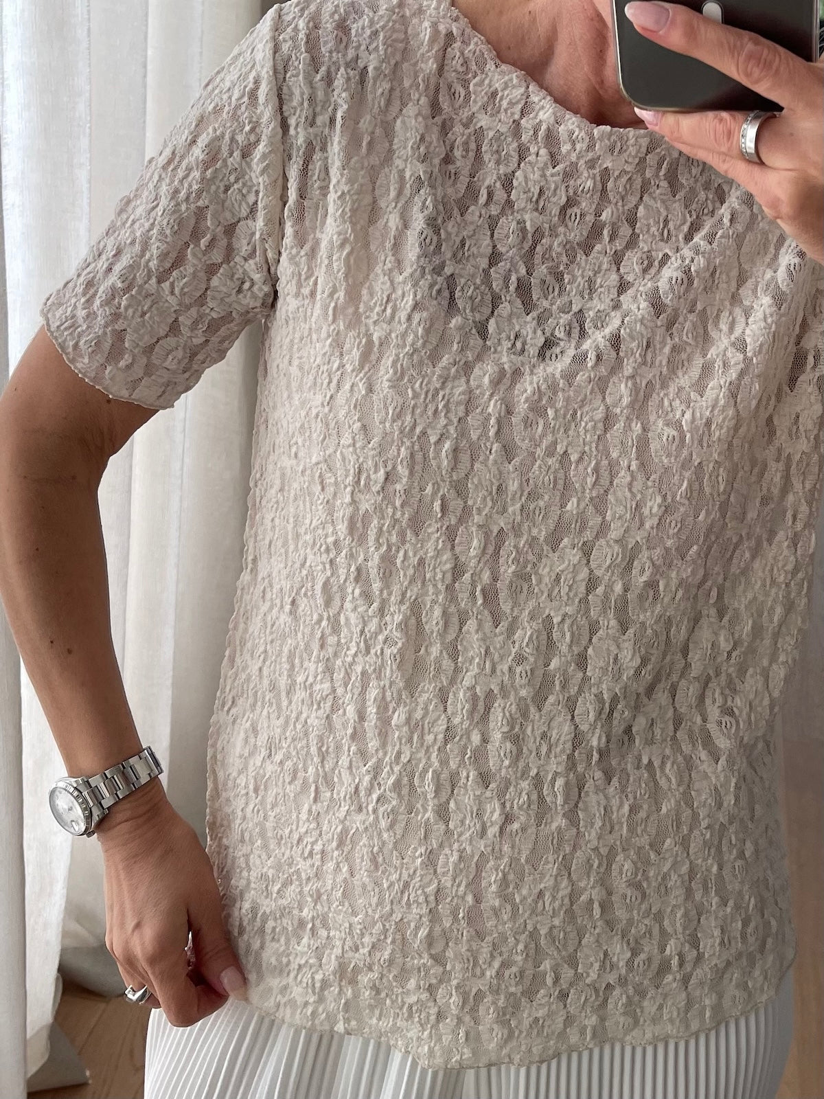 Nahaufnahme des beigefarbenen Spitzenshirts Jade. Fokus auf die aufwendige florale Struktur des Materials aus Polyester und Spandex sowie den flachen Halsausschnitt.