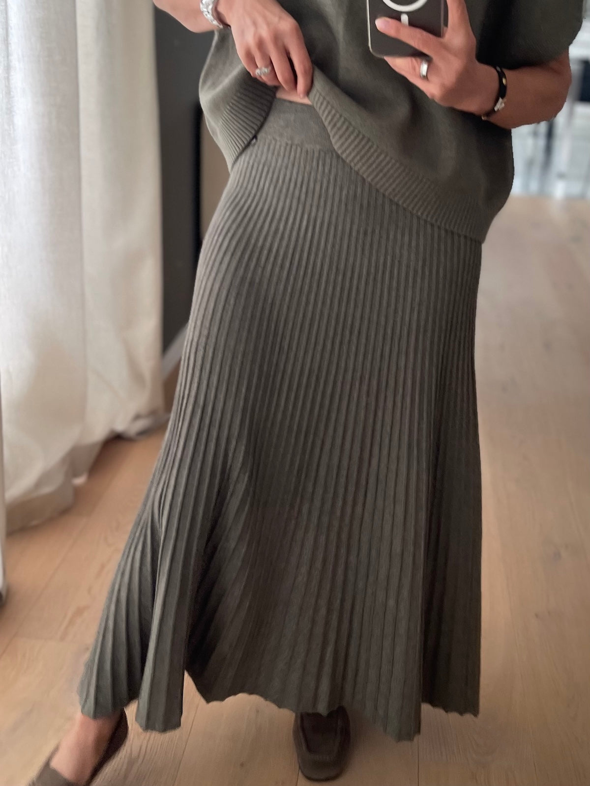 Modebewusste Frau trägt den grünen Strickrock Elise in feiner Plissee-Optik mit einer klar definierten Silhouette, perfekt abgestimmt auf den exakt passenden, grünen Strickpullunder Edda.