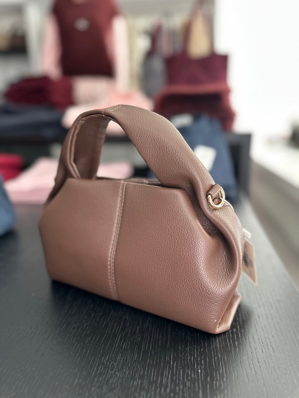 Edle braune Tasche Malia mit klar definierter Linienführung, markantem Tragegriff und goldfarbenen Details, seitliche Ansicht.