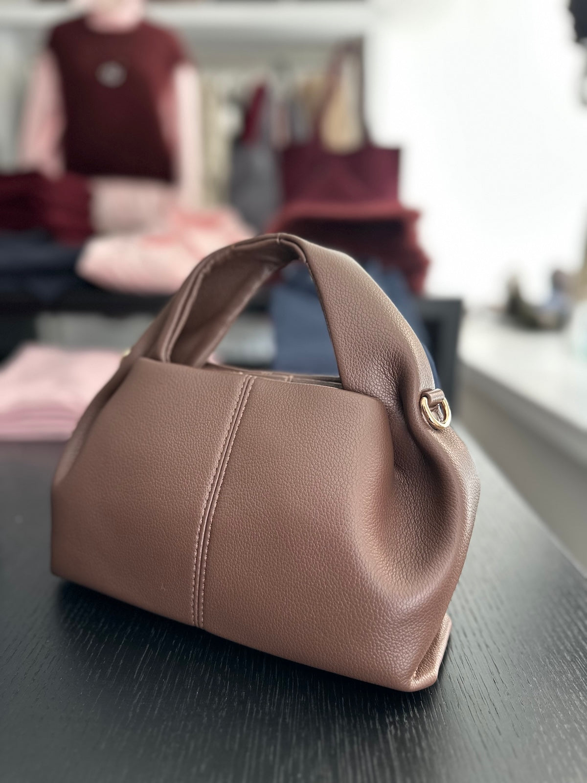 Architektonisch geformte Tasche Malia in edlem Braun, präsentiert im modernen, strukturierten Store-Ambiente.