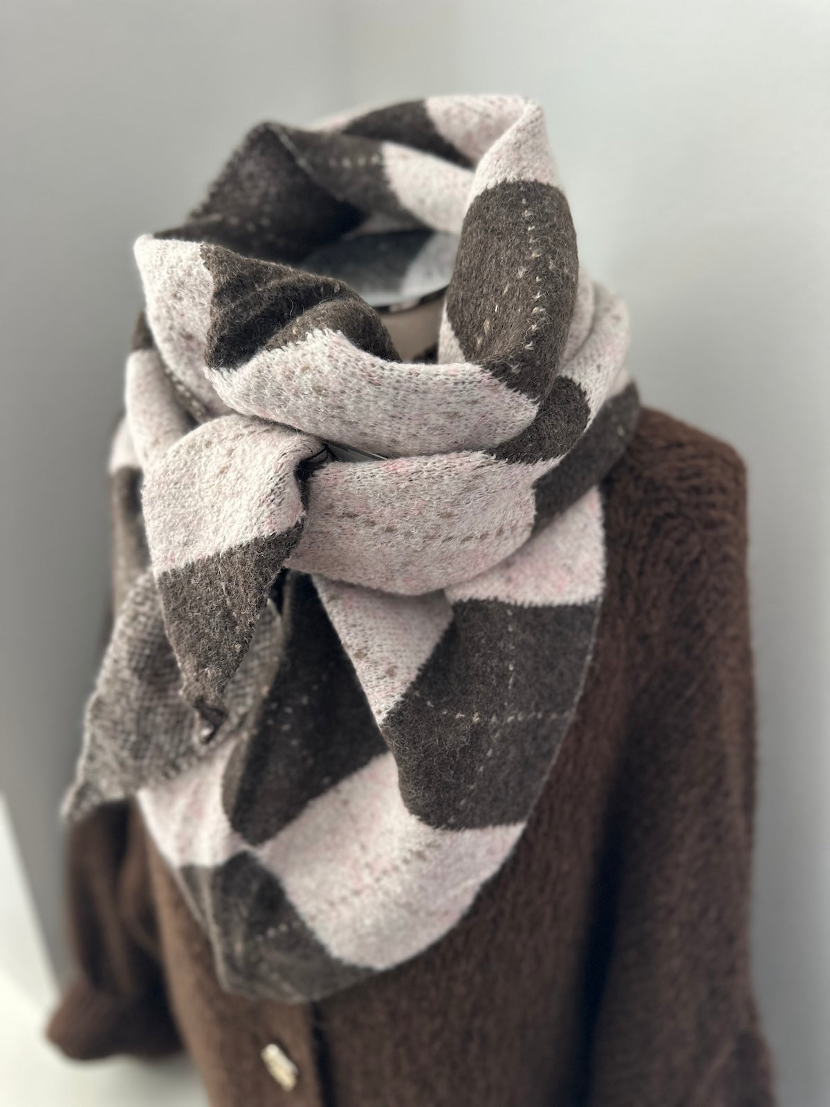 Dreieck-Schal Burlie in Braun und Rosé mit markantem Karo-Muster, strukturiert drapiert auf einer Schaufensterpuppe über einem braunen Strickteil.