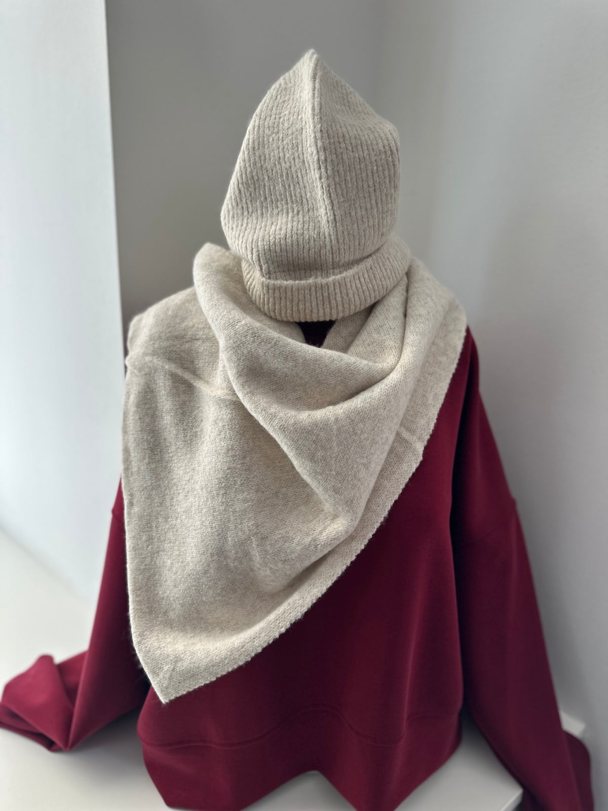 Exklusiver beigefarbener Dreieck-Schal Alma aus 100 % Viscose drapiert auf einer Schaufensterpuppe mit passender gerippter Mütze.