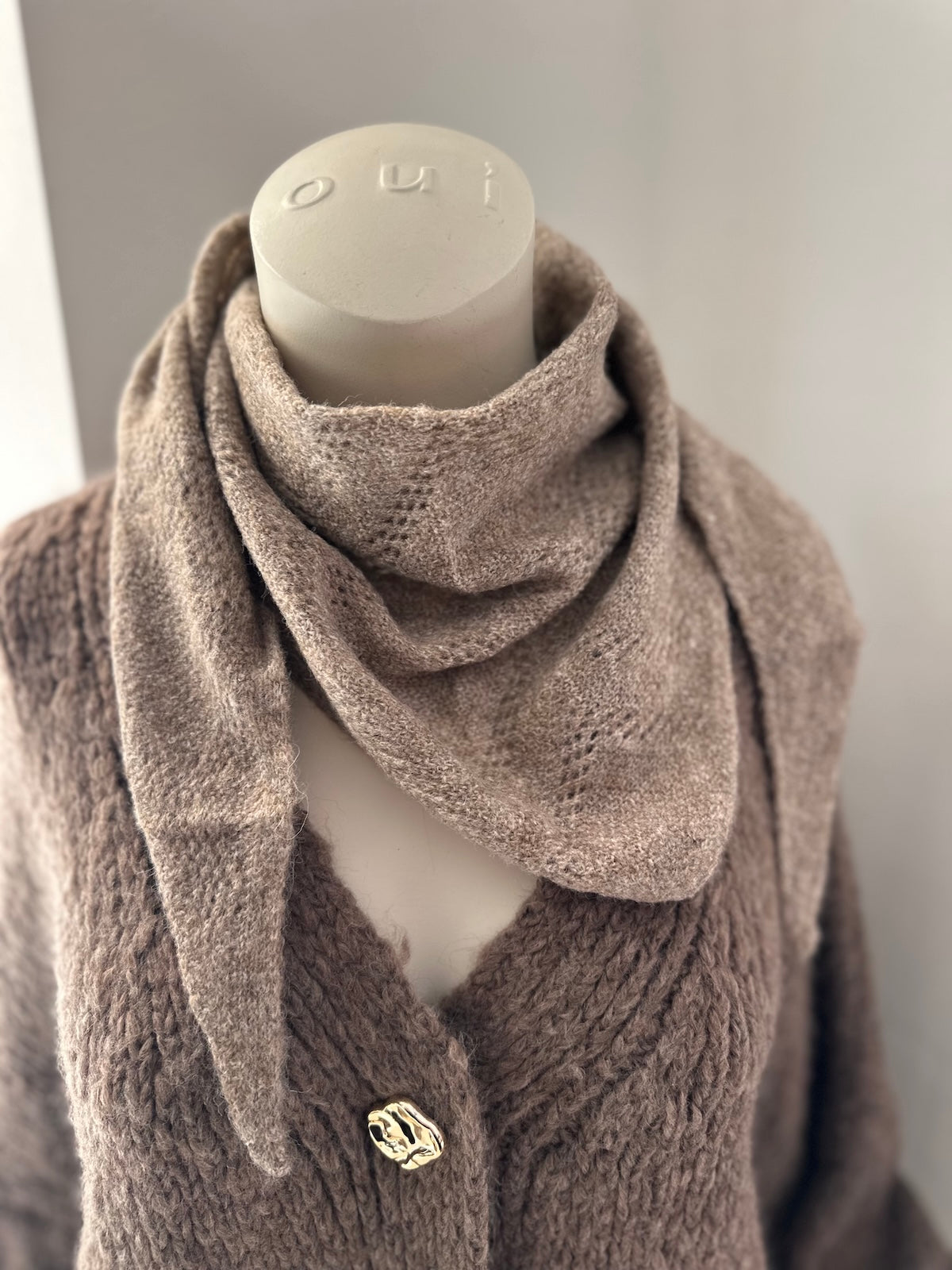 Exklusives taupefarbenes Dreiecks-Tuch Tessa aus 100 % Viscose mit strukturiertem Ajour-Muster, formstabil drapiert auf einer Schaufensterpuppe.