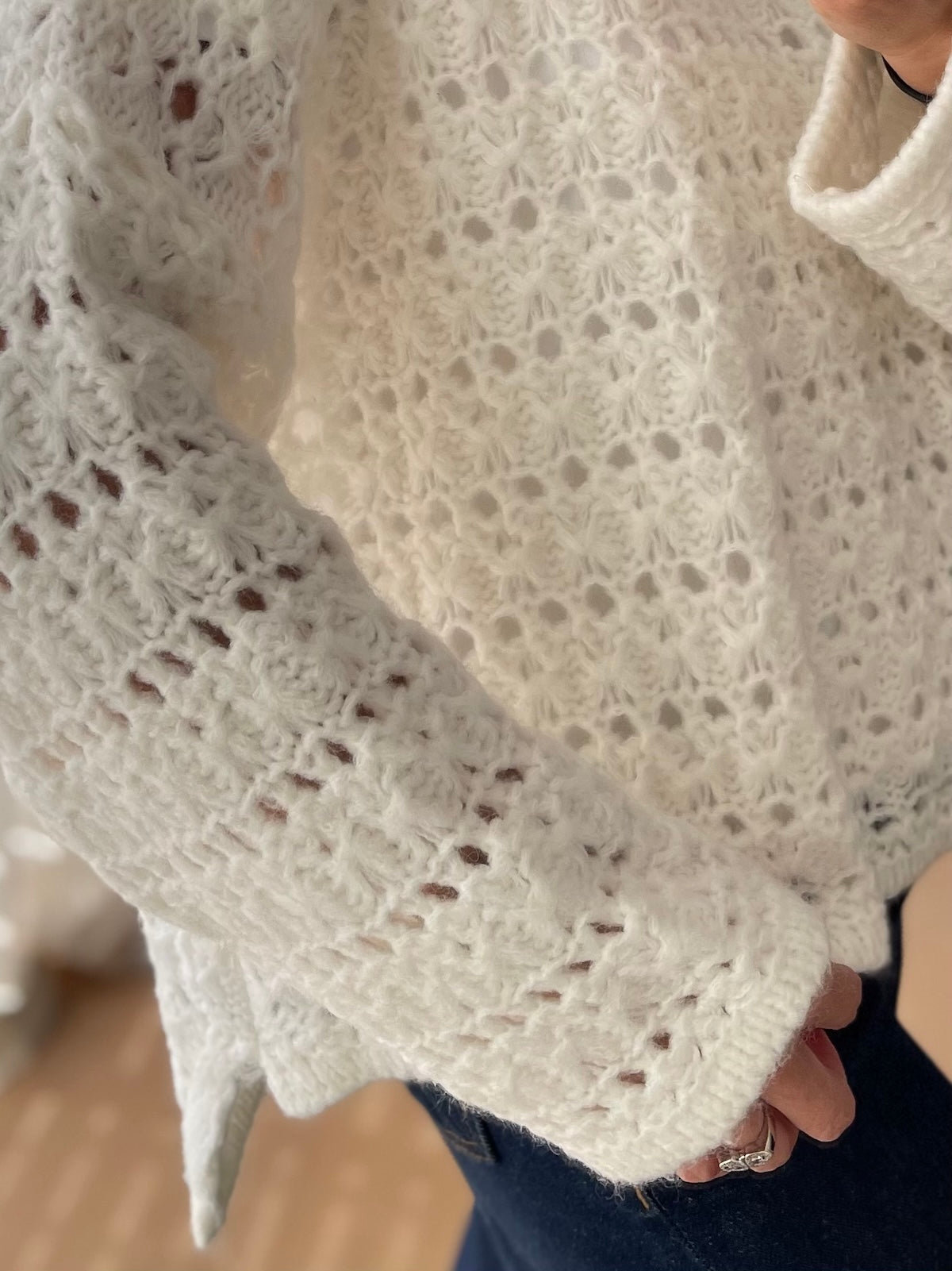 Detailansicht des wollweißen Pullovers Nomi mit Fokus auf die hochwertige, durchbrochene Grobstrick-Struktur und den soften, hochwertigen Maschenfall am Ärmel.