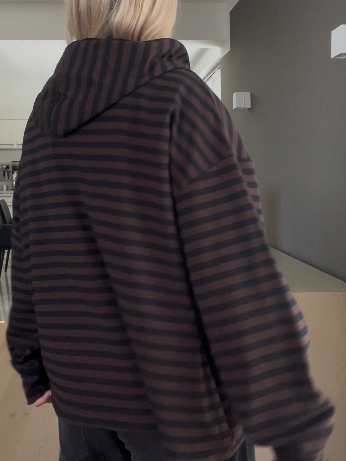 Rückansicht des gestreiften Hoodies Thea in Schoko-Schwarz, die das strukturierte Volumen, die überschnittenen Schultern und den edlen Fall der Kapuze demonstriert.