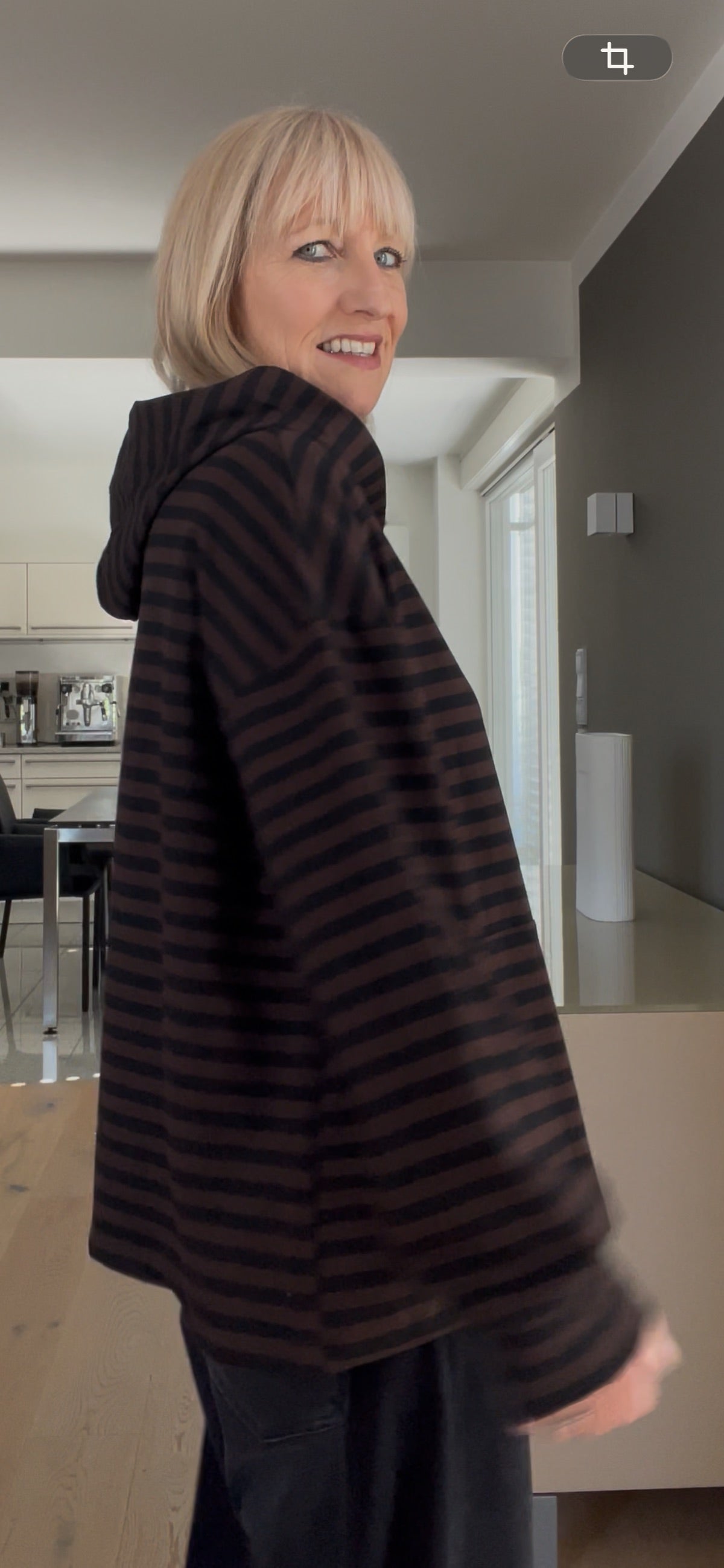 Seitenansicht des gestreiften Hoodies Thea in Schoko-Schwarz, die das strukturierte Volumen, die überschnittenen Schultern und den edlen Fall der Kapuze demonstriert.
