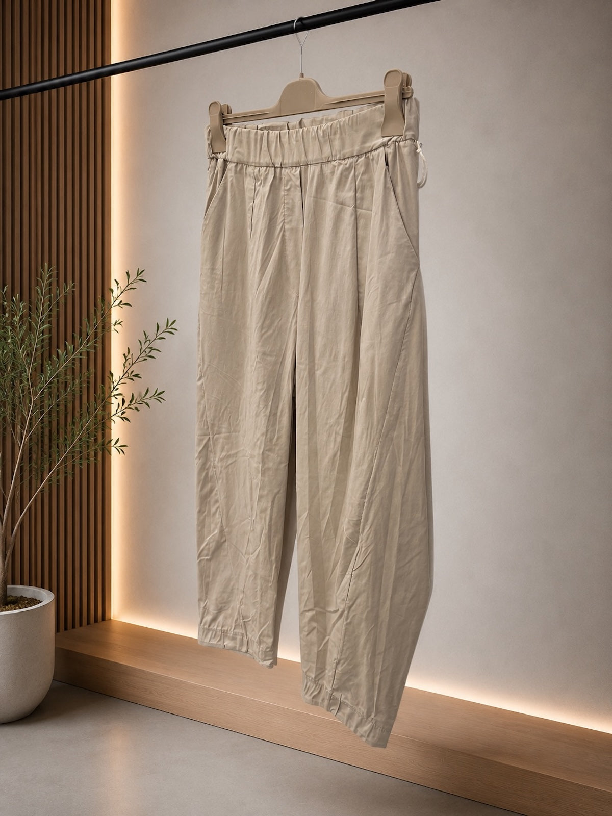 Detailaufnahme der Hose Elisa in Stone auf einem Holzkleiderbügel zur optimalen Darstellung des rundum elastischen Raffbunds und des strukturierten, matt-griffigen Materials.