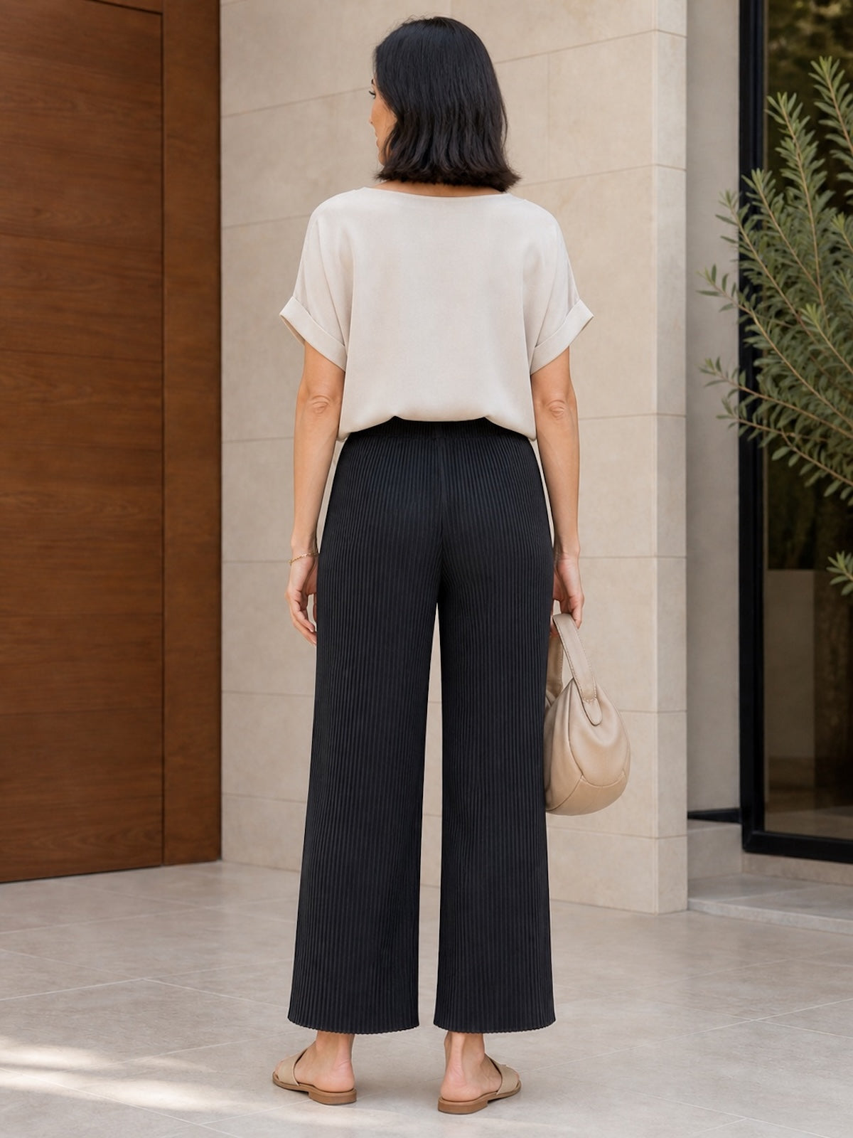Rückansicht der eleganten, schwarzen Plissee-Hose Tony. Die fehlenden Gesäßtaschen sorgen für eine extrem cleane, fließende Silhouette, kombiniert mit einem hellen Oberteil.
