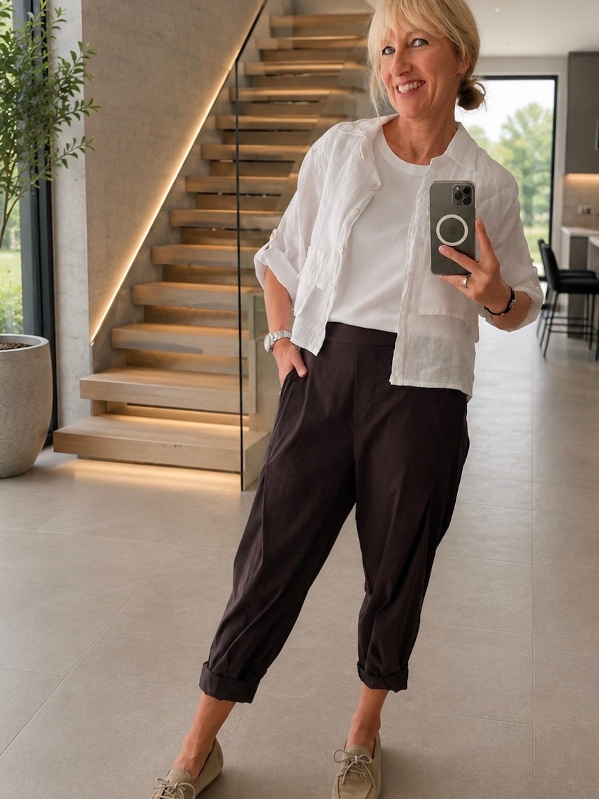 Vorderansicht der sportlich-eleganten Hose Larissa in Dunkelbraun an einem Modell, kombiniert mit einer weißen Bluse und flachen Schuhen in Beige.