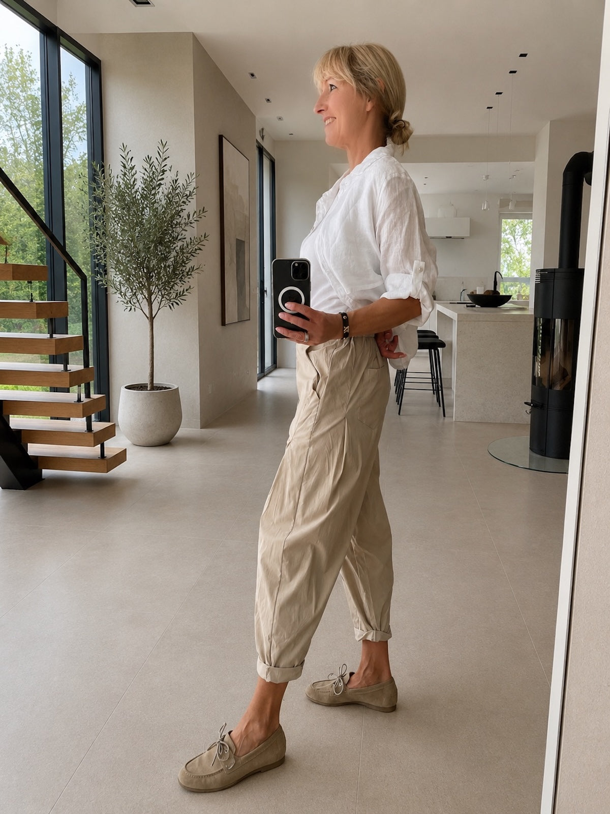 Seitenansicht der beigen Hose Larissa in Stone im modernen Loft, die den edlen, blusigen Fall des Stoffes und die verkürzte Cropped-Silhouette mit gekrempeltem Saum zeigt