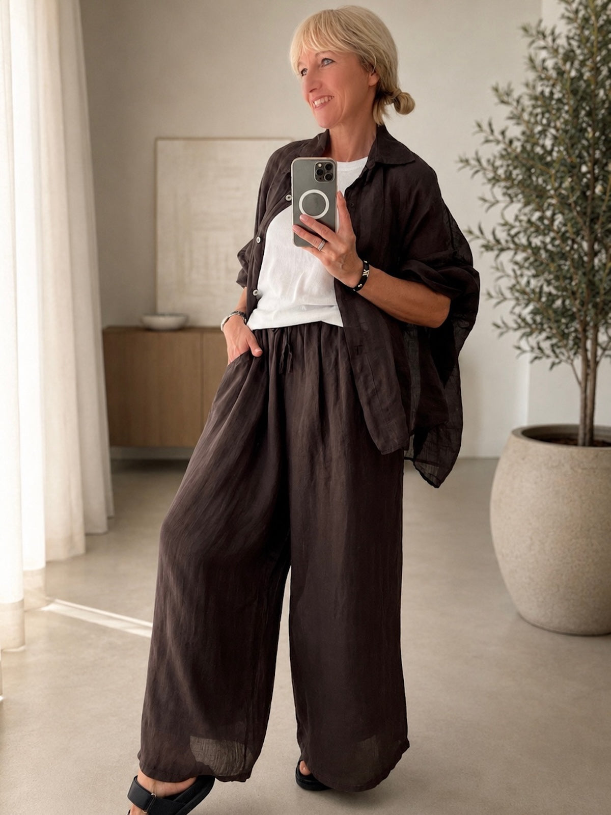 Seitenprofil des Modells in der schokobraunen Leinen-Hose Ariella zur optimalen Veranschaulichung der edlen, fließenden Beinsilhouette und des strukturierten Leinenmaterials.