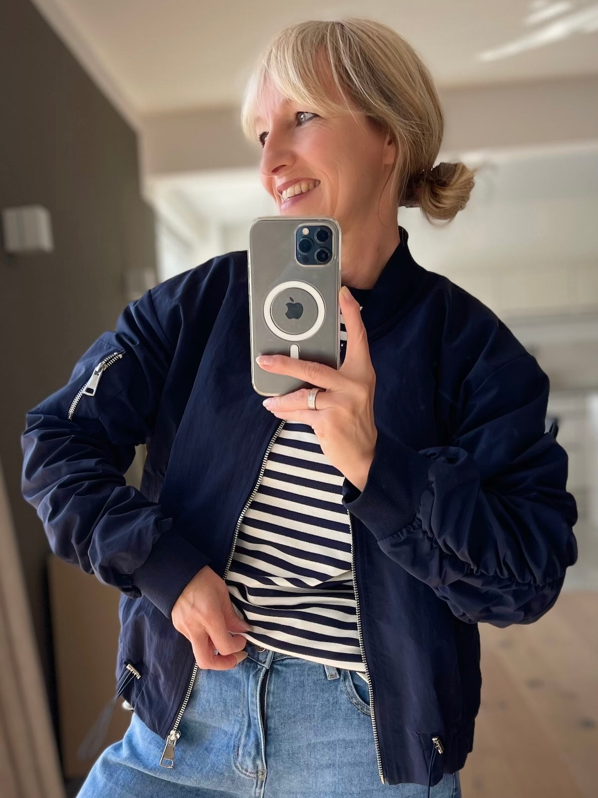 Model präsentiert die lässige blaue Bomberjacke Barbara im sportlichen Look mit gerafften Ärmeln und einem maritim gestreiften Oberteil.