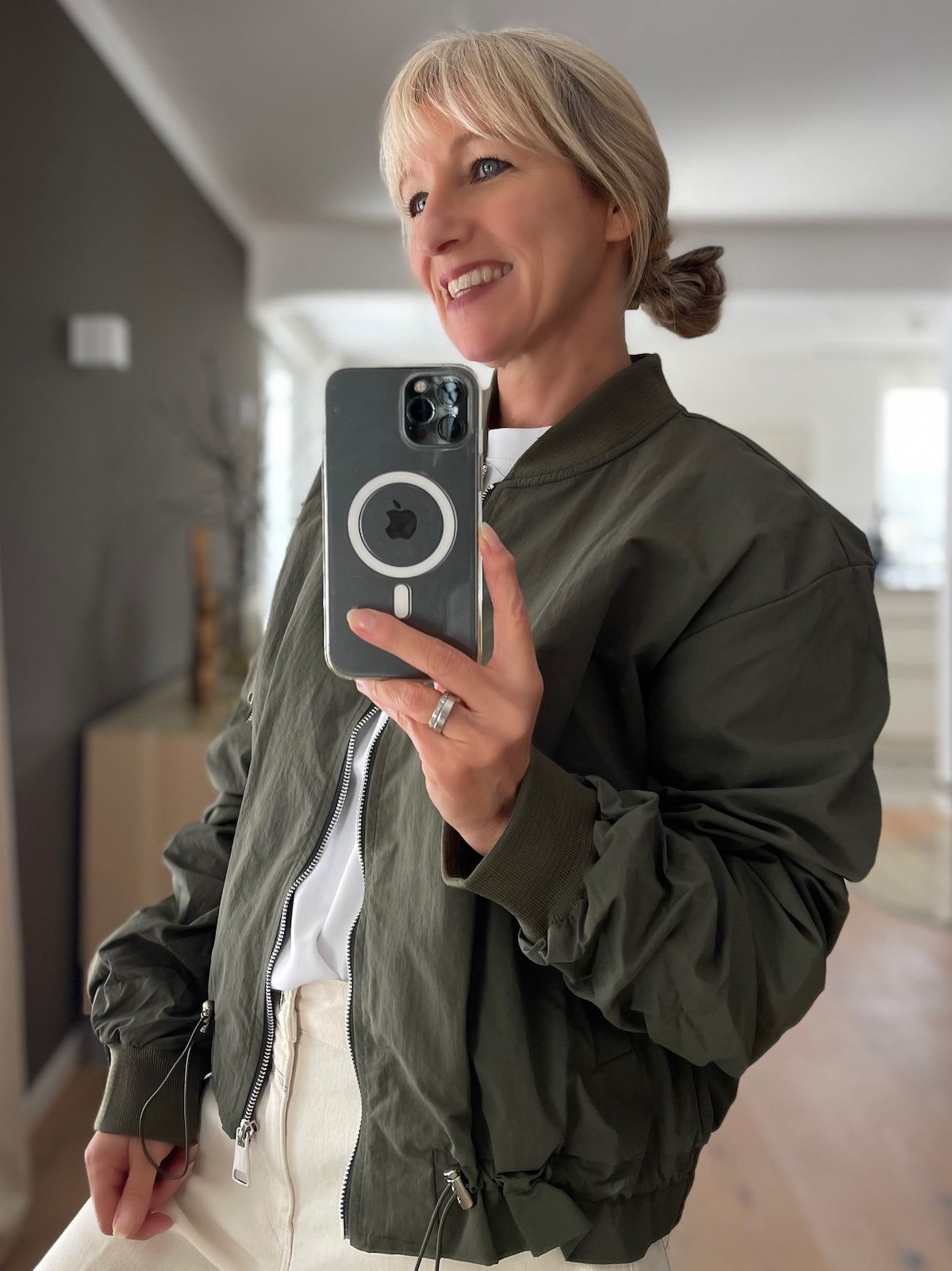 Model fotografiert sich im Spiegel in einer sportlich-eleganten grünen Bomberjacke Barbara und einer hellen Hose.