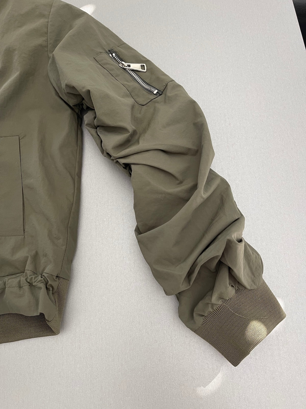 Ärmel einer grünen Damen-Bomberjacke Barbara aus Nylon mit aufgesetzter Reißverschlusstasche und Rippstrickbündchen.