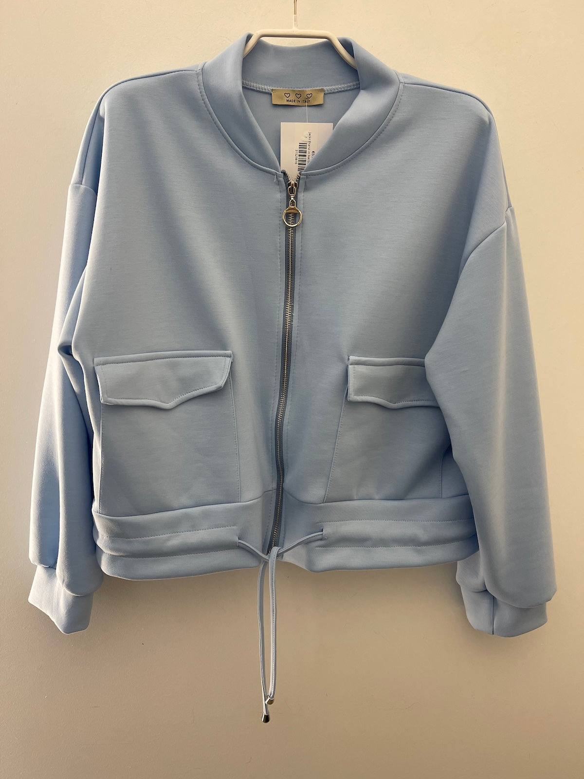 Hellblaue Damenjacke Franzi (Made in Italy) im Bomber-Stil mit silbernem Ring-Reißverschluss und Tunnelzug am Saum, fotografiert auf einem weißen Kleiderbügel.