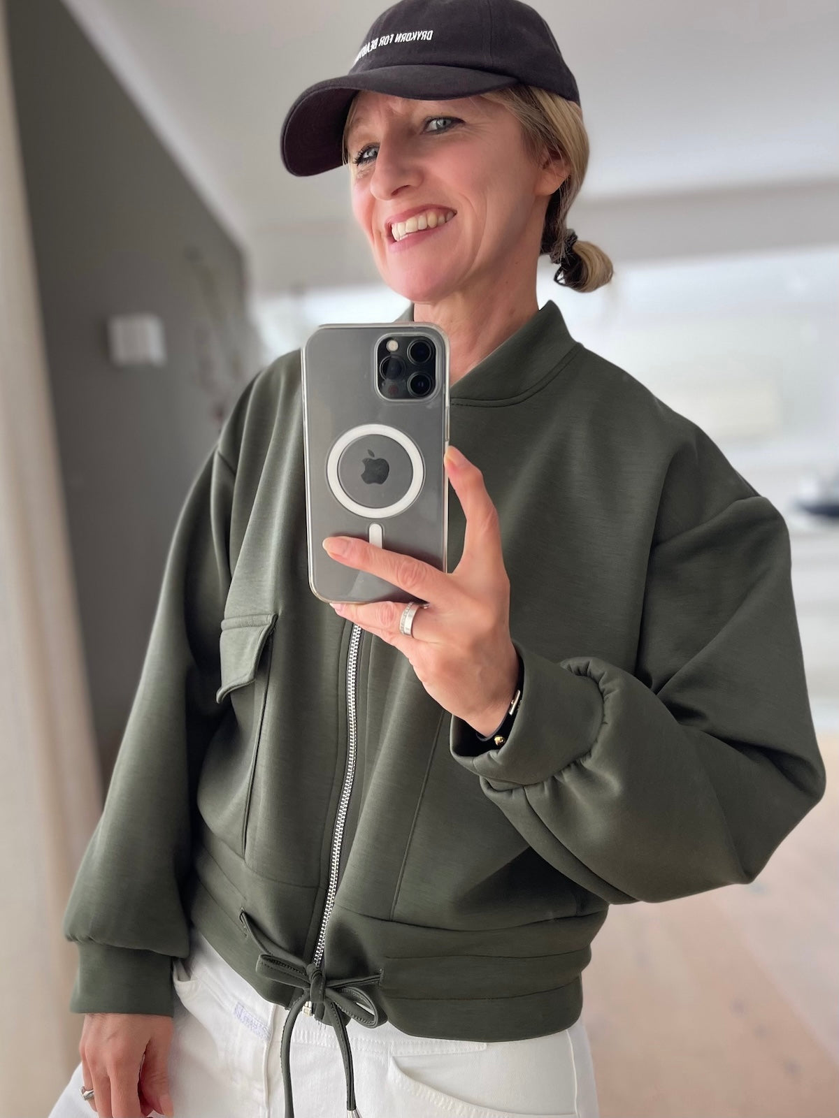 Sportliche Damen Jacke Franzi in Grün mit Reißverschluss und Kordelzug am Saum kombiniert mit weißer Hose und Cap