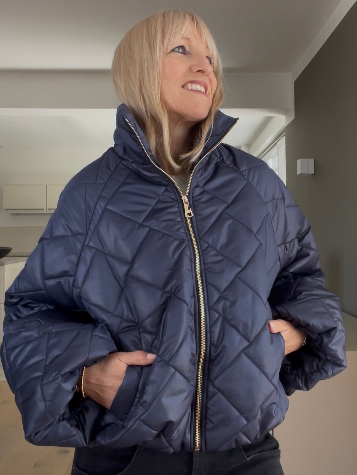 Eine modebewusste Frau trägt die dunkelblaue Jacke Jany mit edlem Rauten-Steppmuster, gestylt im strukturierten Cropped-Schnitt mit weiten Ärmeln und goldfarbenem Reißverschluss