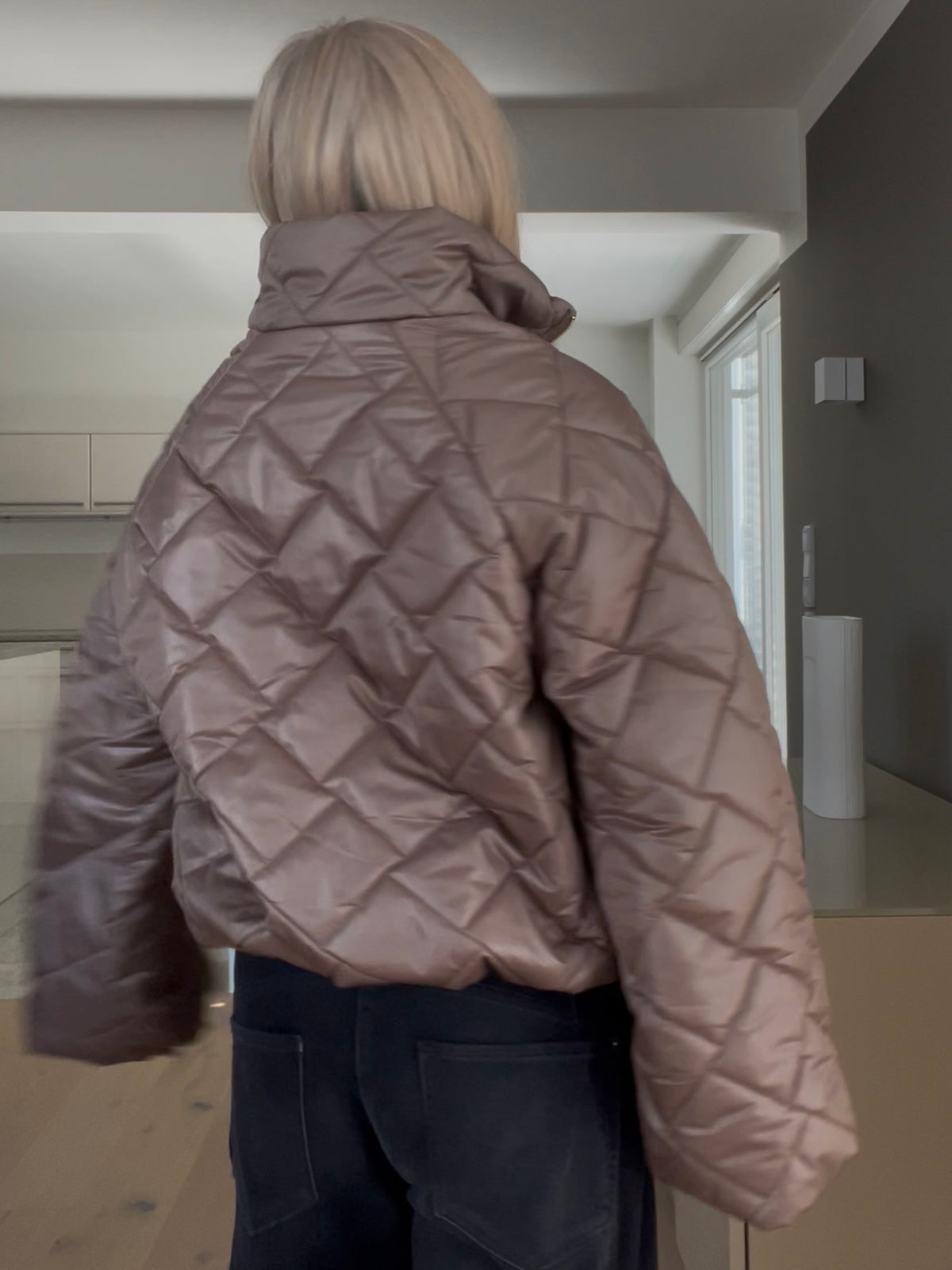 Rückansicht der Jacke Jany in der Trendfarbe Taupe mit edlem Rauten-Steppmuster, gestylt im strukturierten Cropped-Schnitt mit weiten Ärmeln und goldfarbenem Reißverschluss.