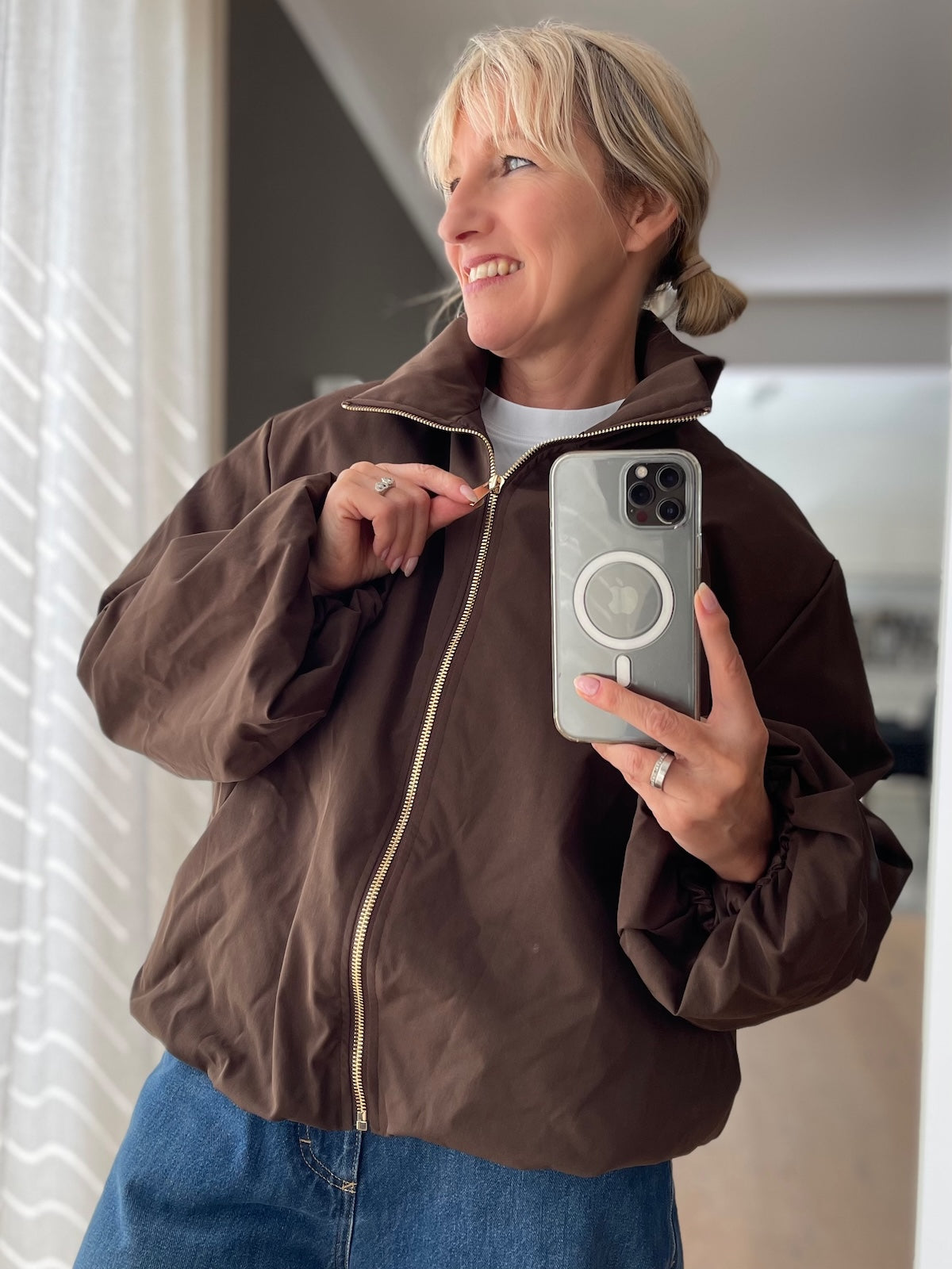 Dame präsentiert die elegante Jacke Sofia in edlem Braun mit goldfarbenem Reißverschluss im modernen Boxy-Style.
