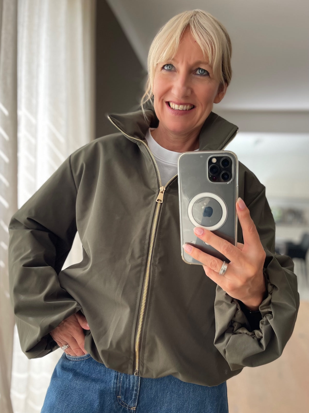 Dame präsentiert die elegante Jacke Sofia in ausdrucksstarkem Oliv mit goldfarbenem Reißverschluss im modernen Boxy-Style.
