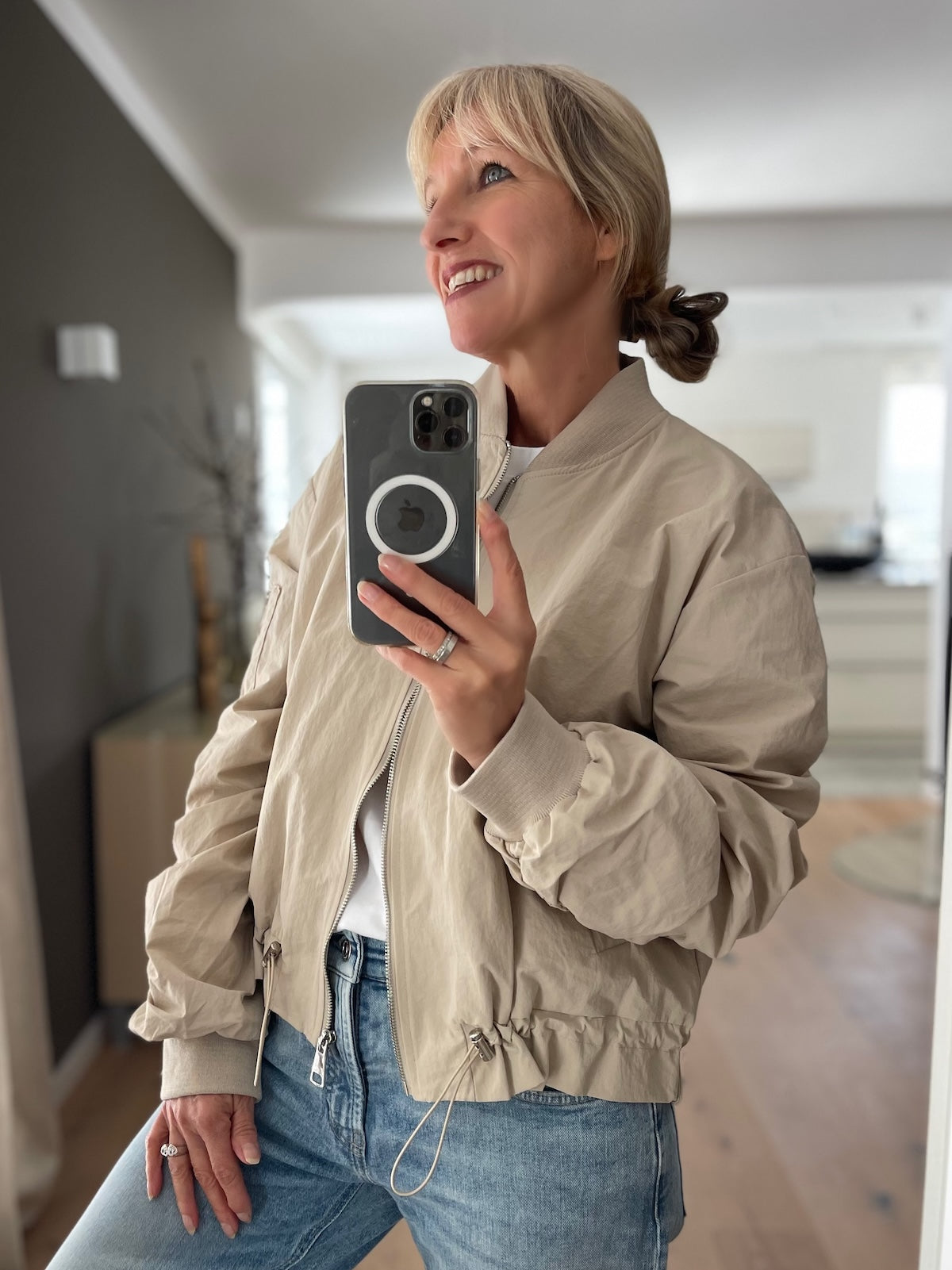 Frontansicht der sportlichen Damen-Kapuzenjacke Barbara in der hellen Farbe Stone, kombiniert mit einer coolen Jeans. Die markanten Klappentaschen und der hochschließende Kragen sind gut sichtbar.
